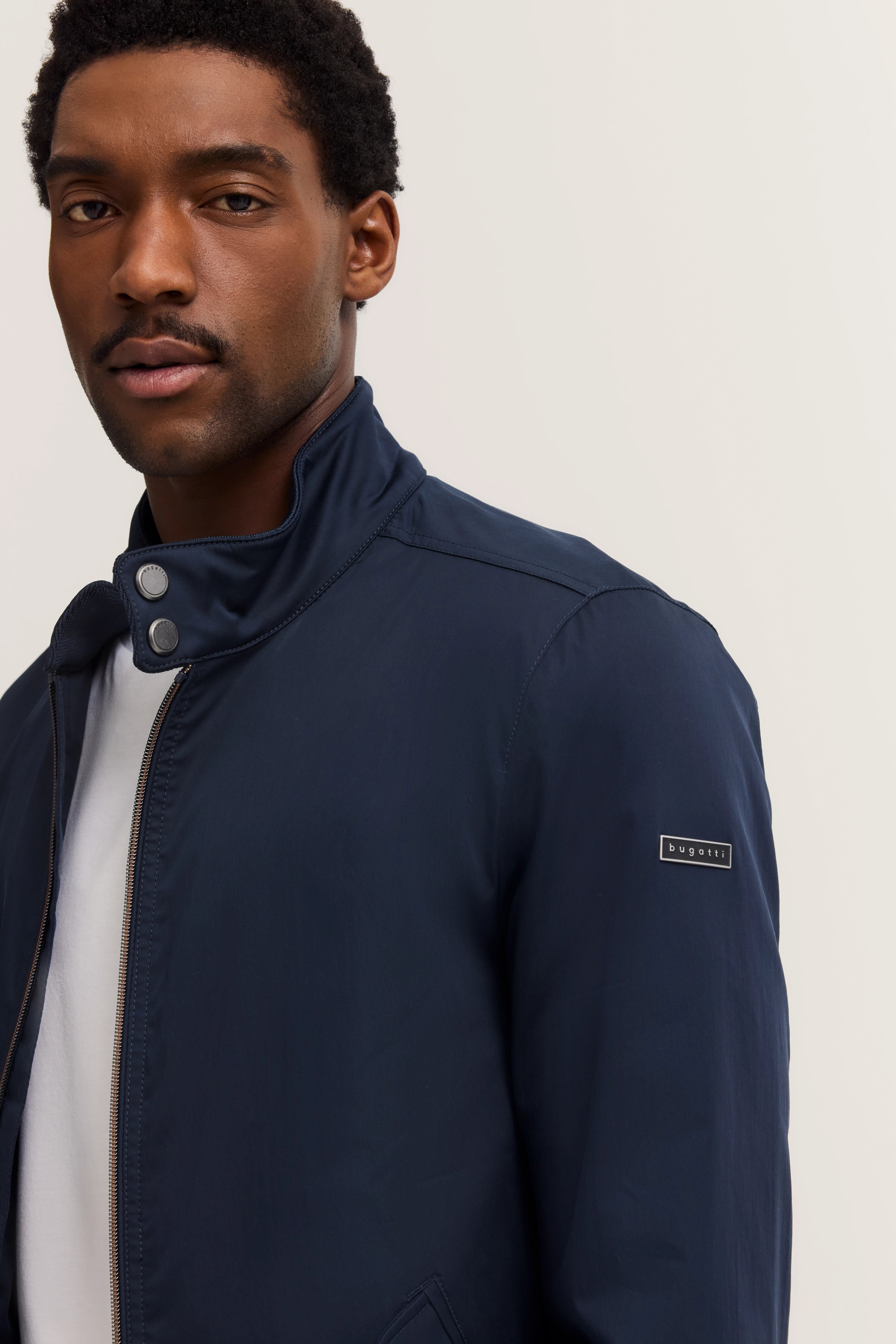 bugatti modelbeeld: Man in donkerblauwe jas met opstaande kraag, nonchalant poserend, stijlvol en elegant.