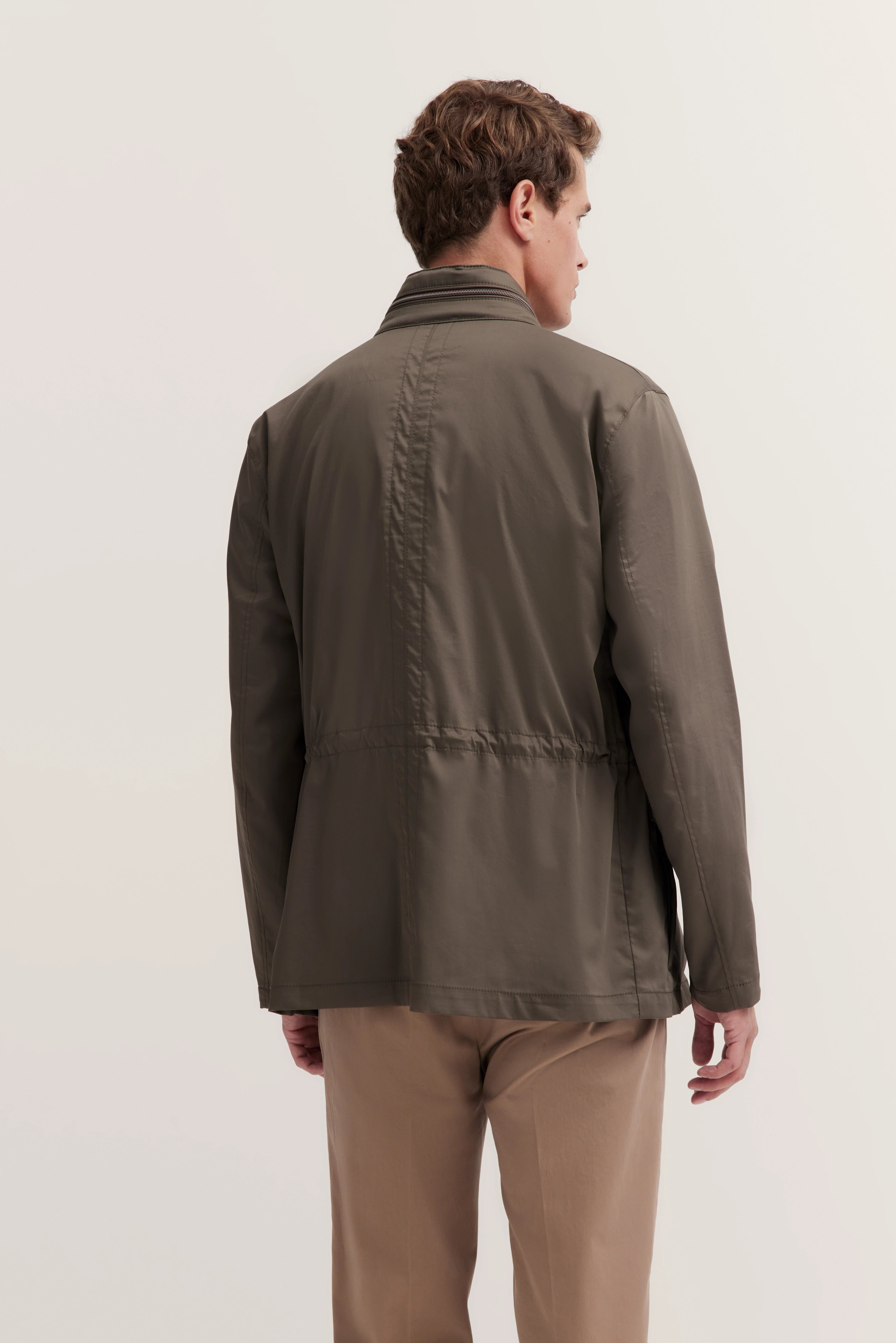 Model in bugatti jas, olijfgroen, en beige broek, achteraanzicht. Ontspannen, casual pose.