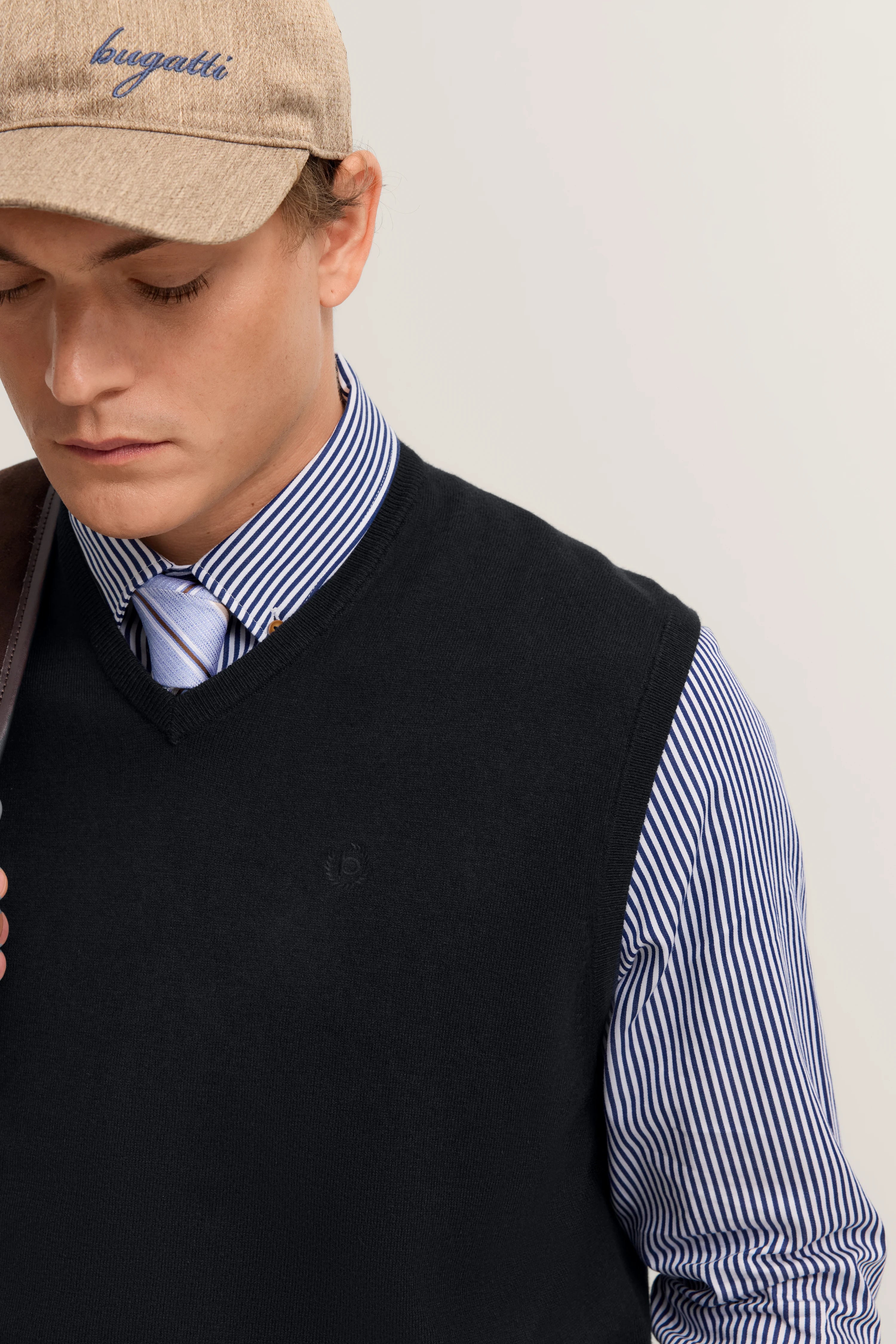 "Modelbild: Mann in gestreiftem Hemd, schwarzer Weste und bugatti-Basecap, neutraler Ausdruck."