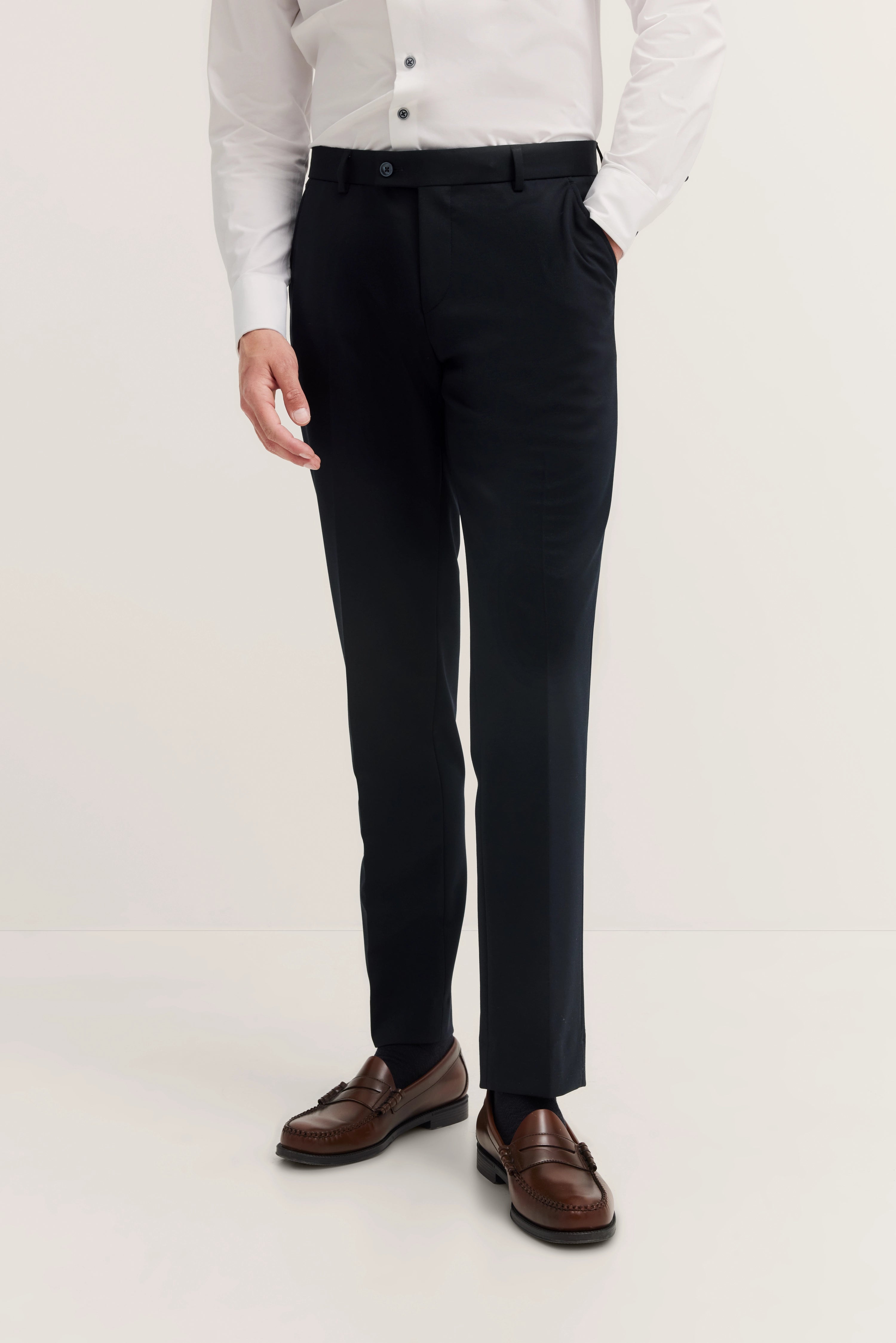 Elegant model image: White shirt, black trousers, brown loafers. Hands relaxed in pockets.
