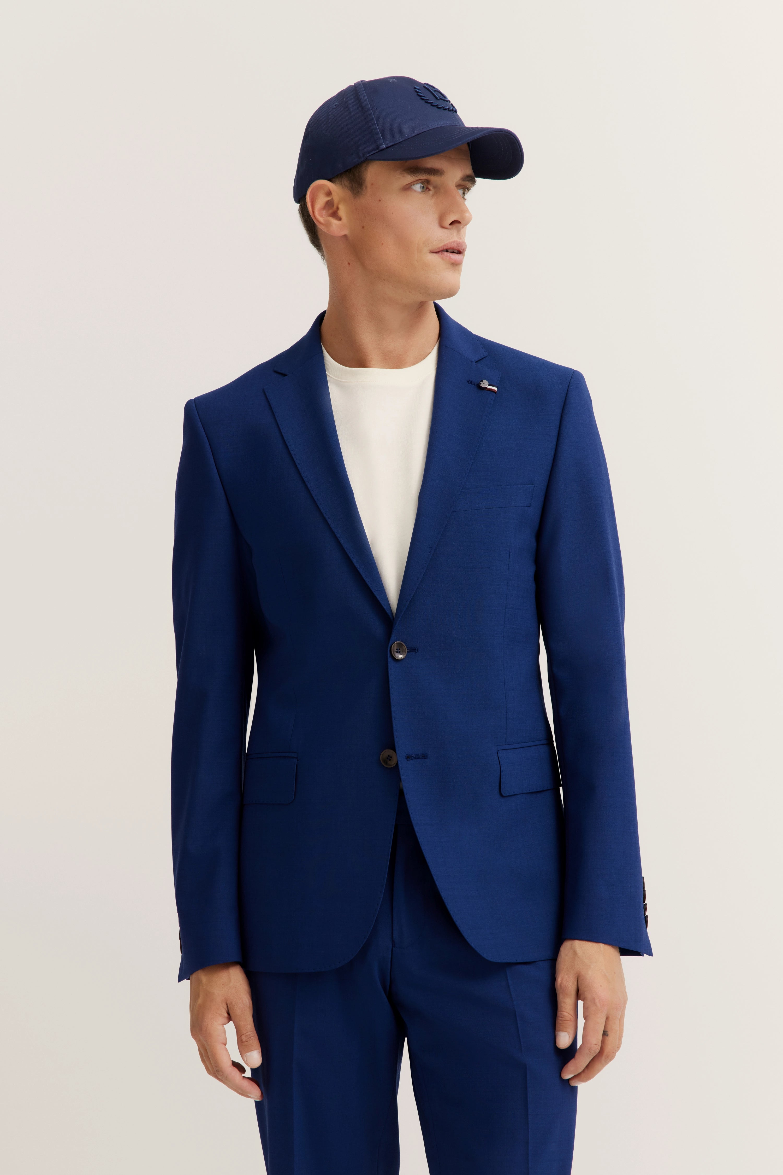 Blue bugatti suit with white shirt and matching cap, model in casual pose.