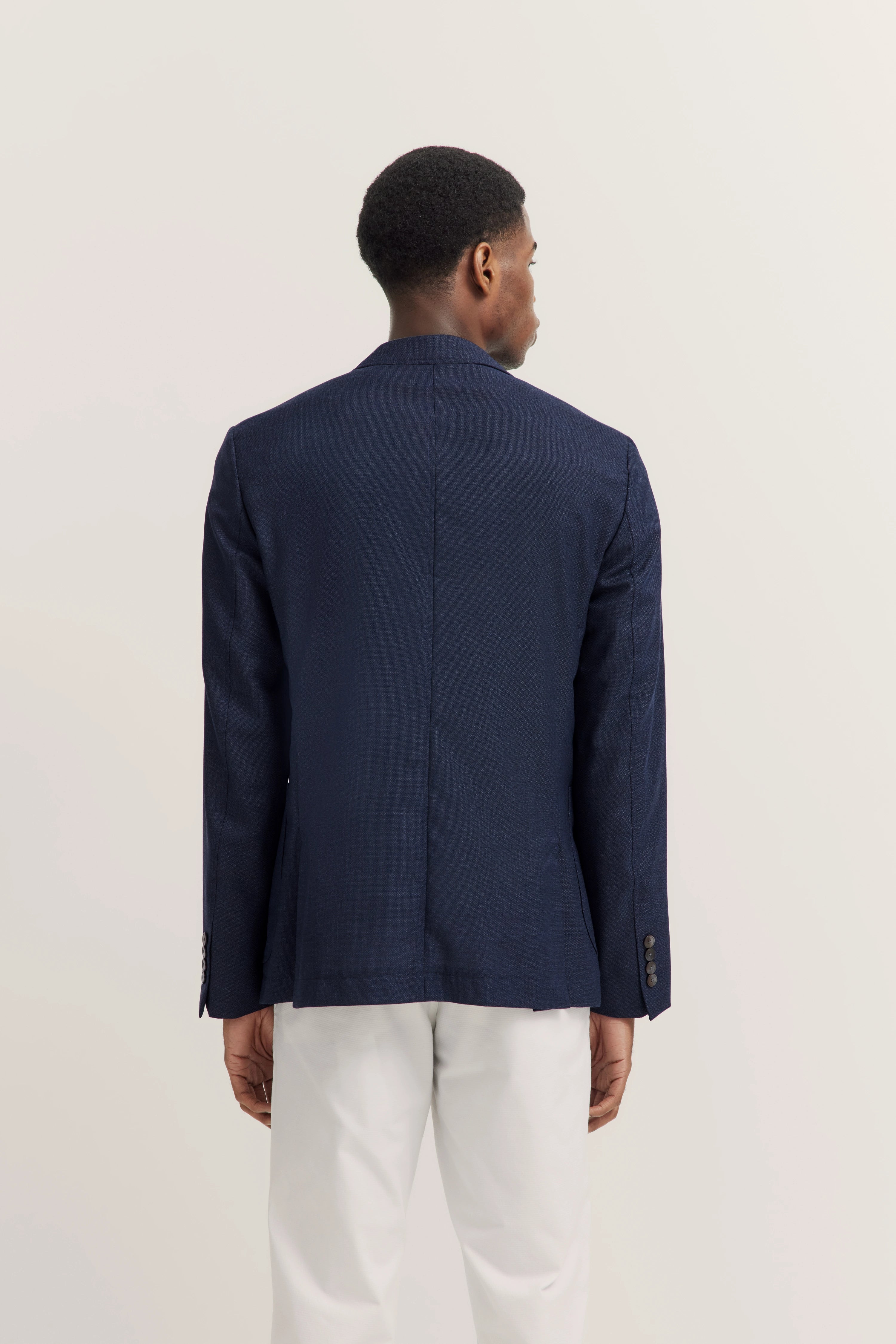 Achterkant van model in donkerblauw bugatti jasje en witte broek.