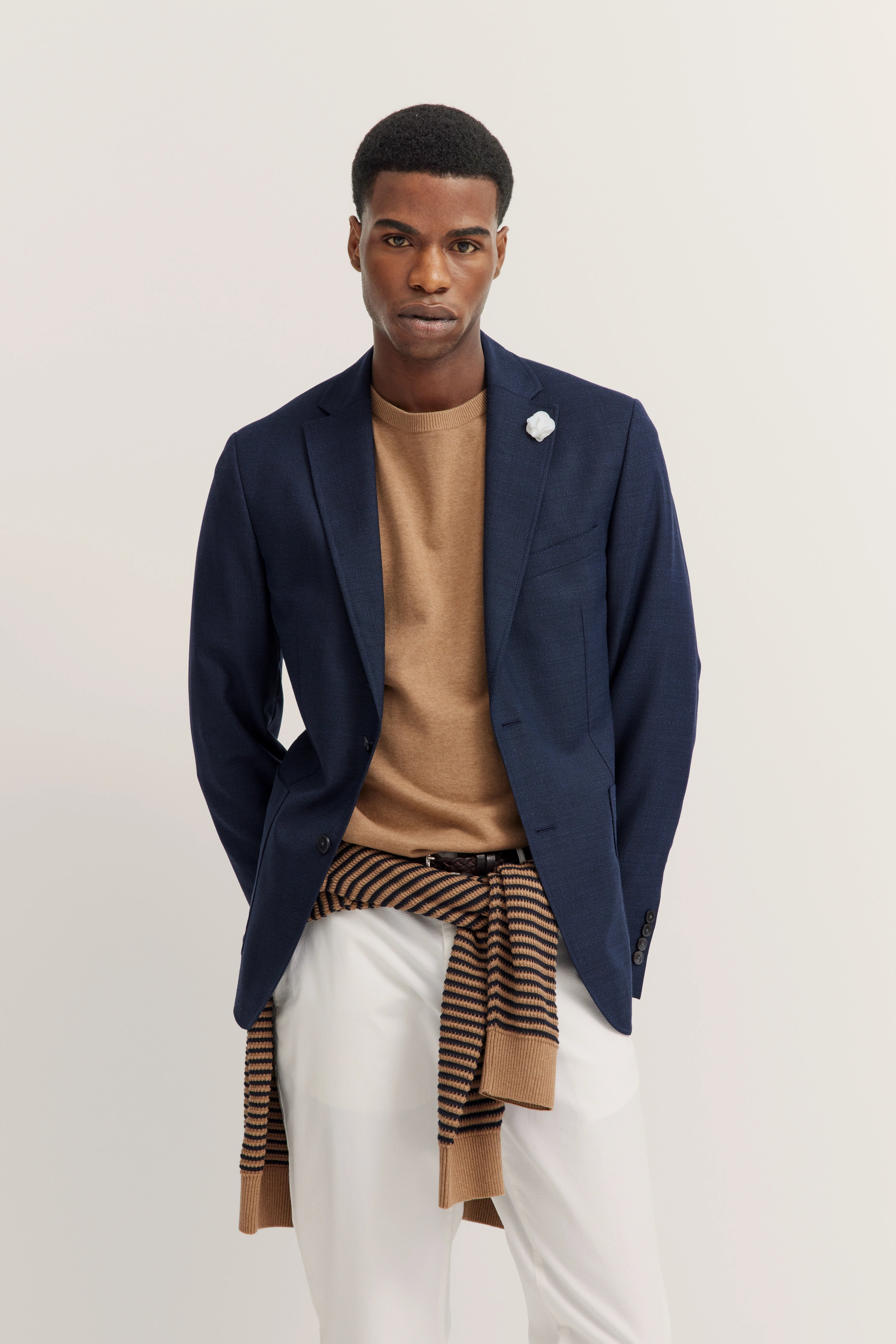 bugatti Model in blauem Blazer, beigem Pullover, weißer Hose und gestreiftem Schal, legeres Posing.