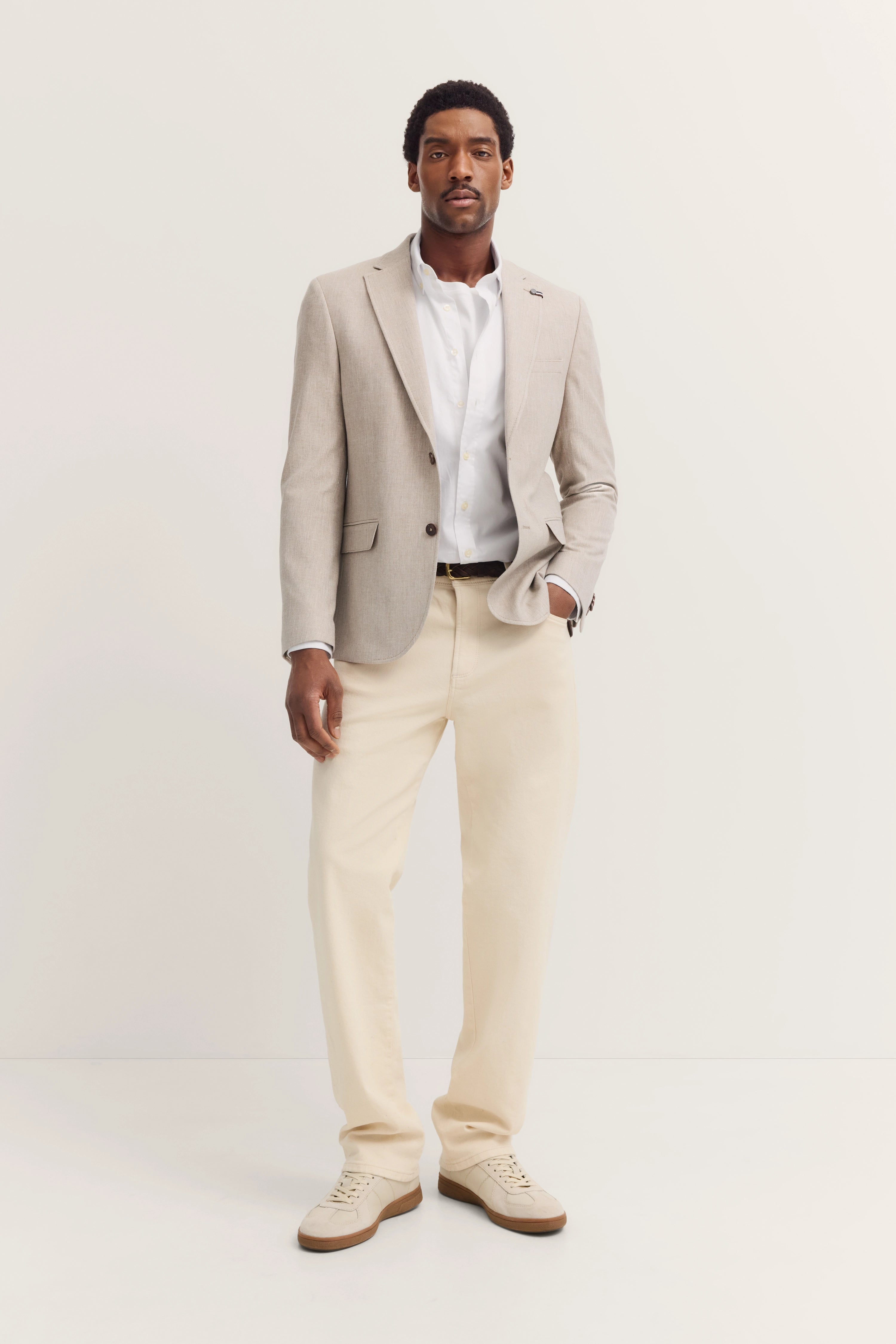 Model in beige bugatti blazer, white shirt, cream trousers, casual pose.