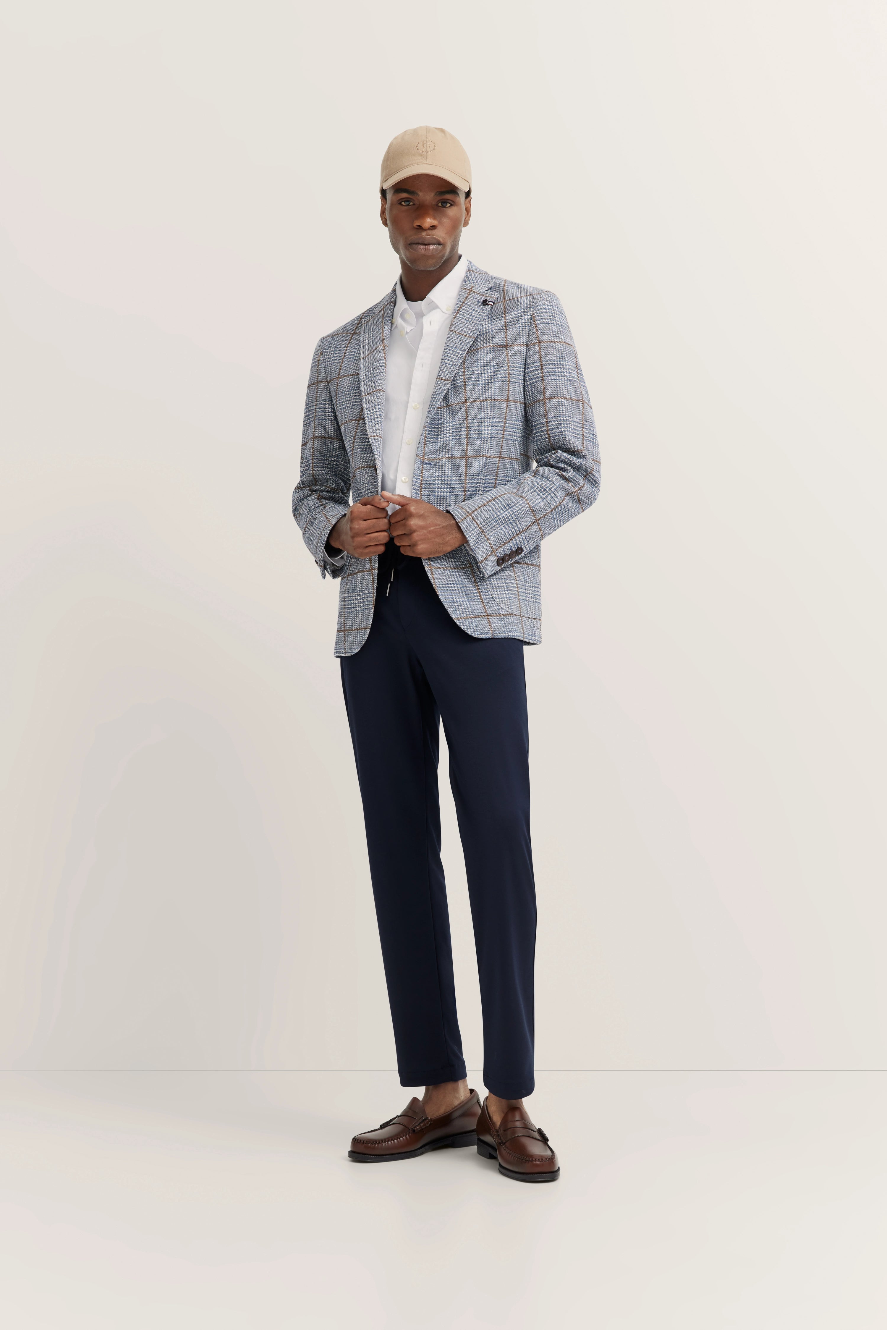 Model in kariertem bugatti Sakko, weißem Hemd, blauer Hose, braunen Schuhen