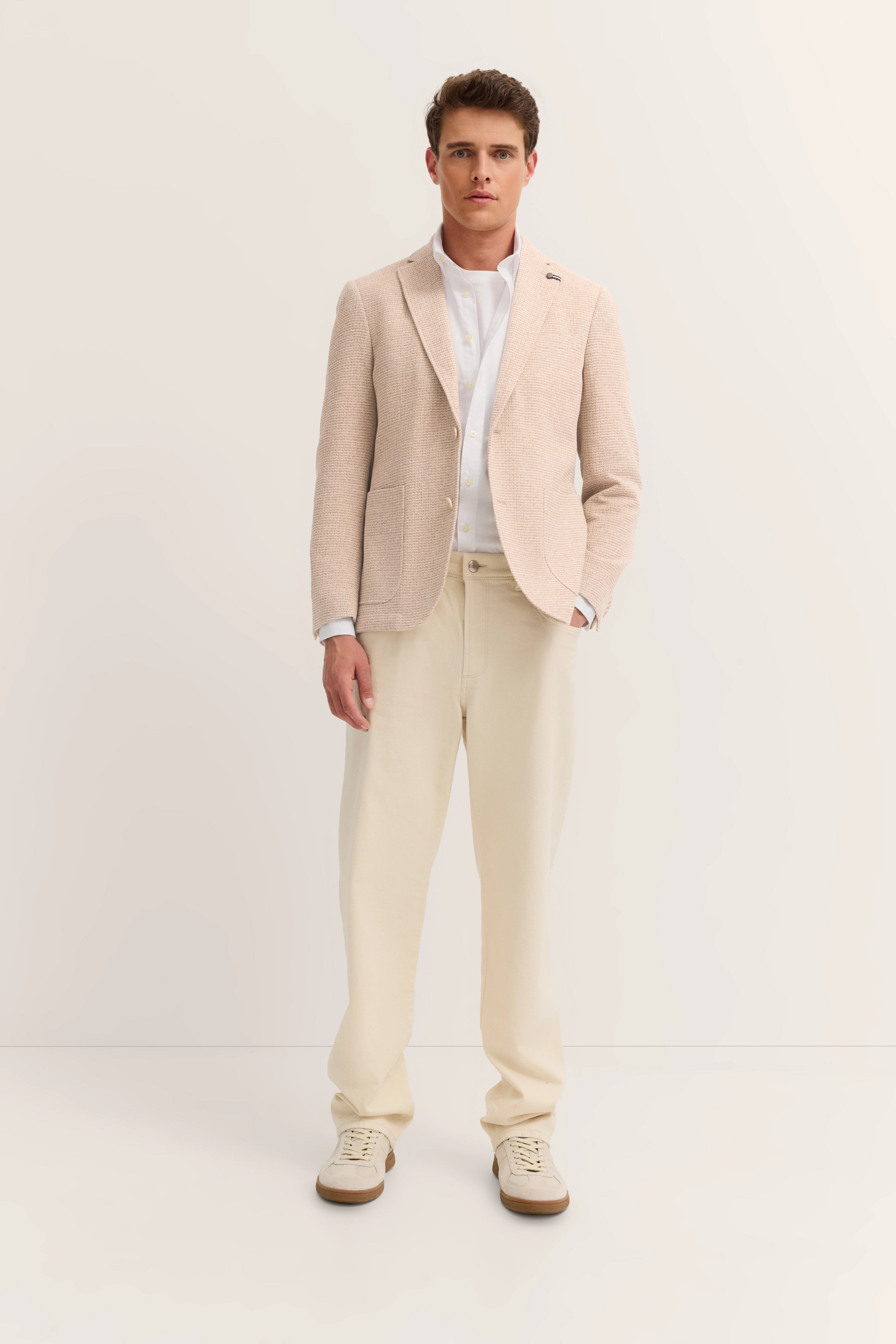 Eleganter Look mit beigem bugatti Blazer, weißem Hemd und cremefarbener Hose. Model stehend, frontal.