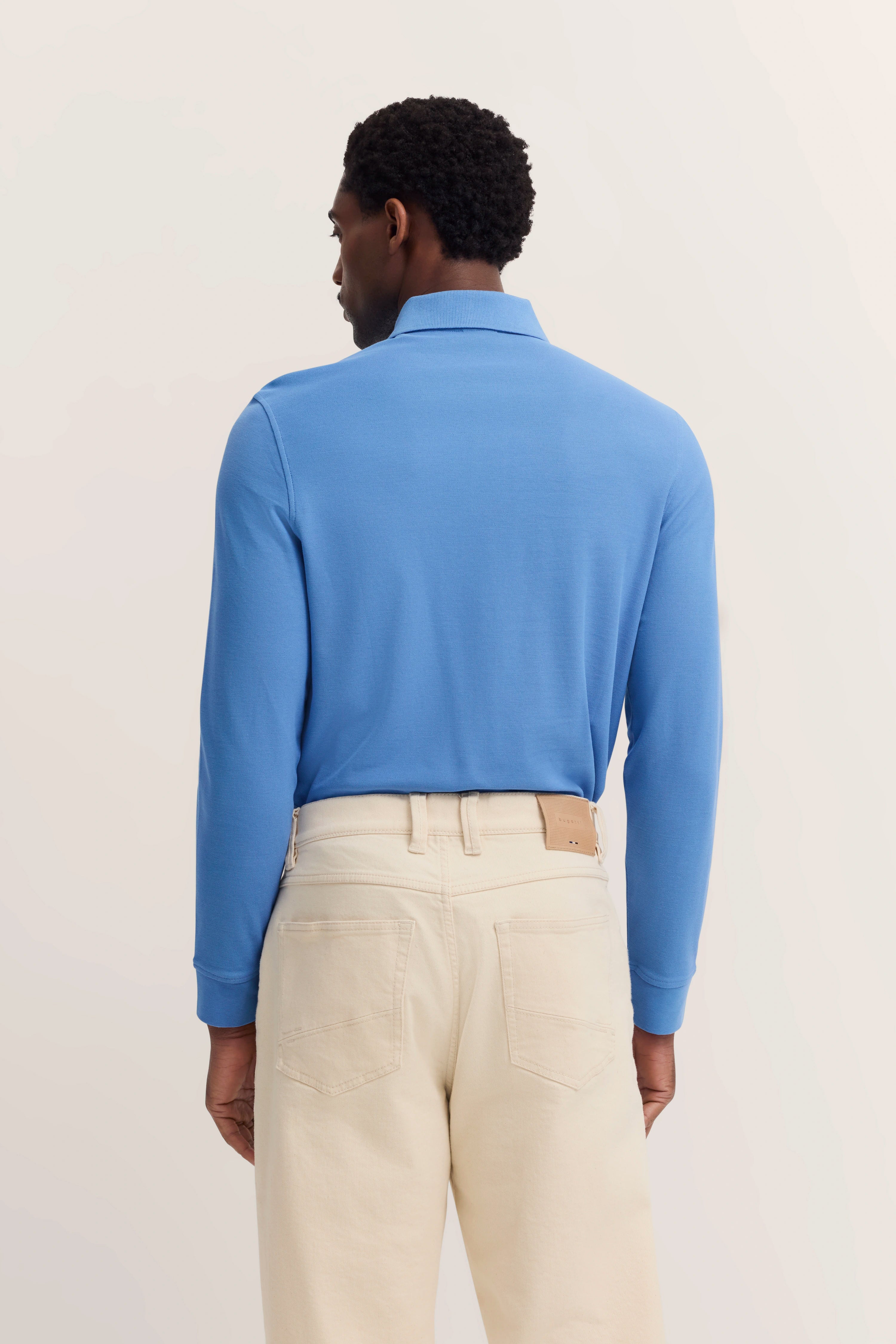 Blue bugatti long-sleeve shirt, beige pants, rear view, casual model pose, relaxed stance.