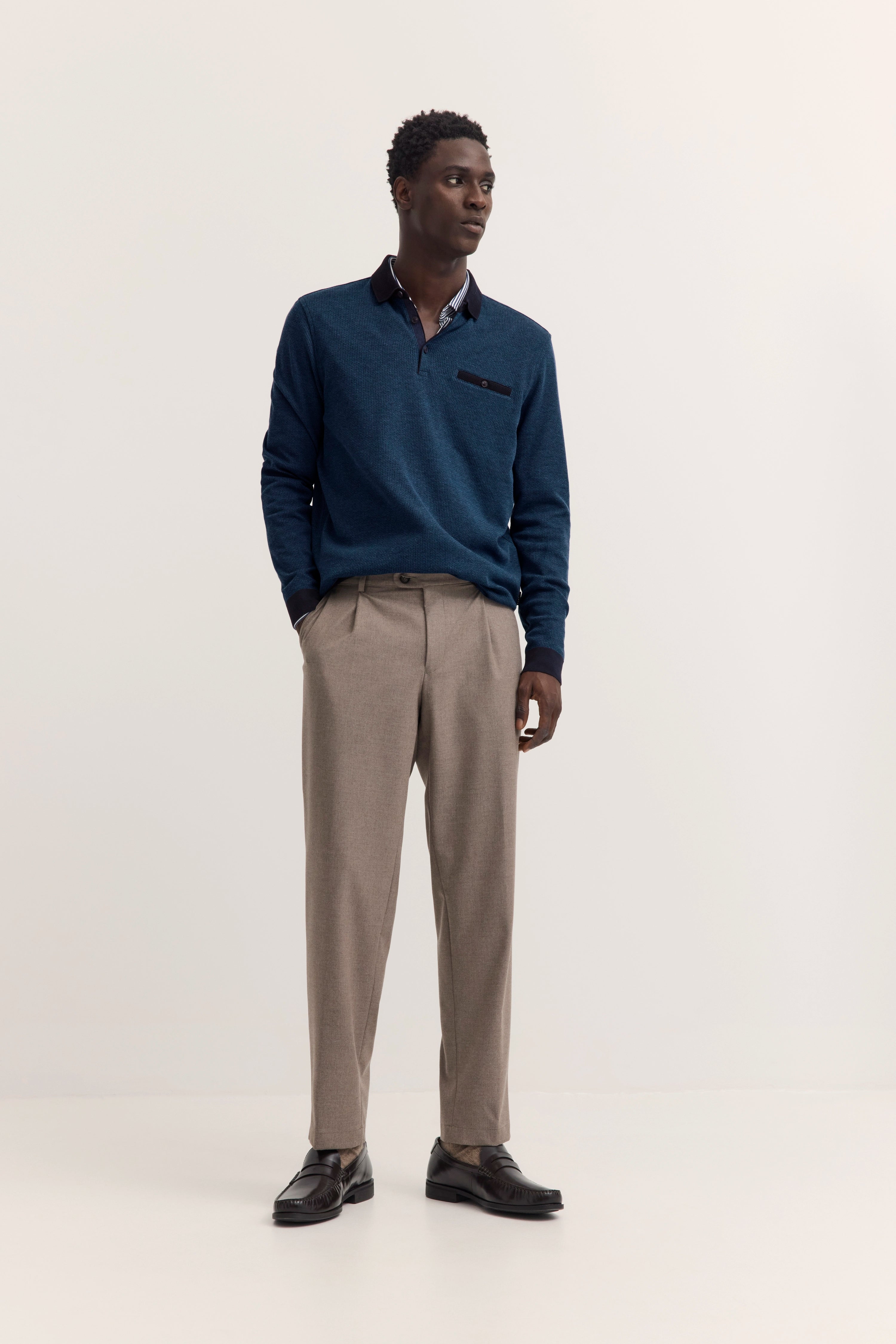 bugatti Modelbild: Mann im blauen Pullover, beiger Hose, schwarze Schuhe, entspanntes Posing.