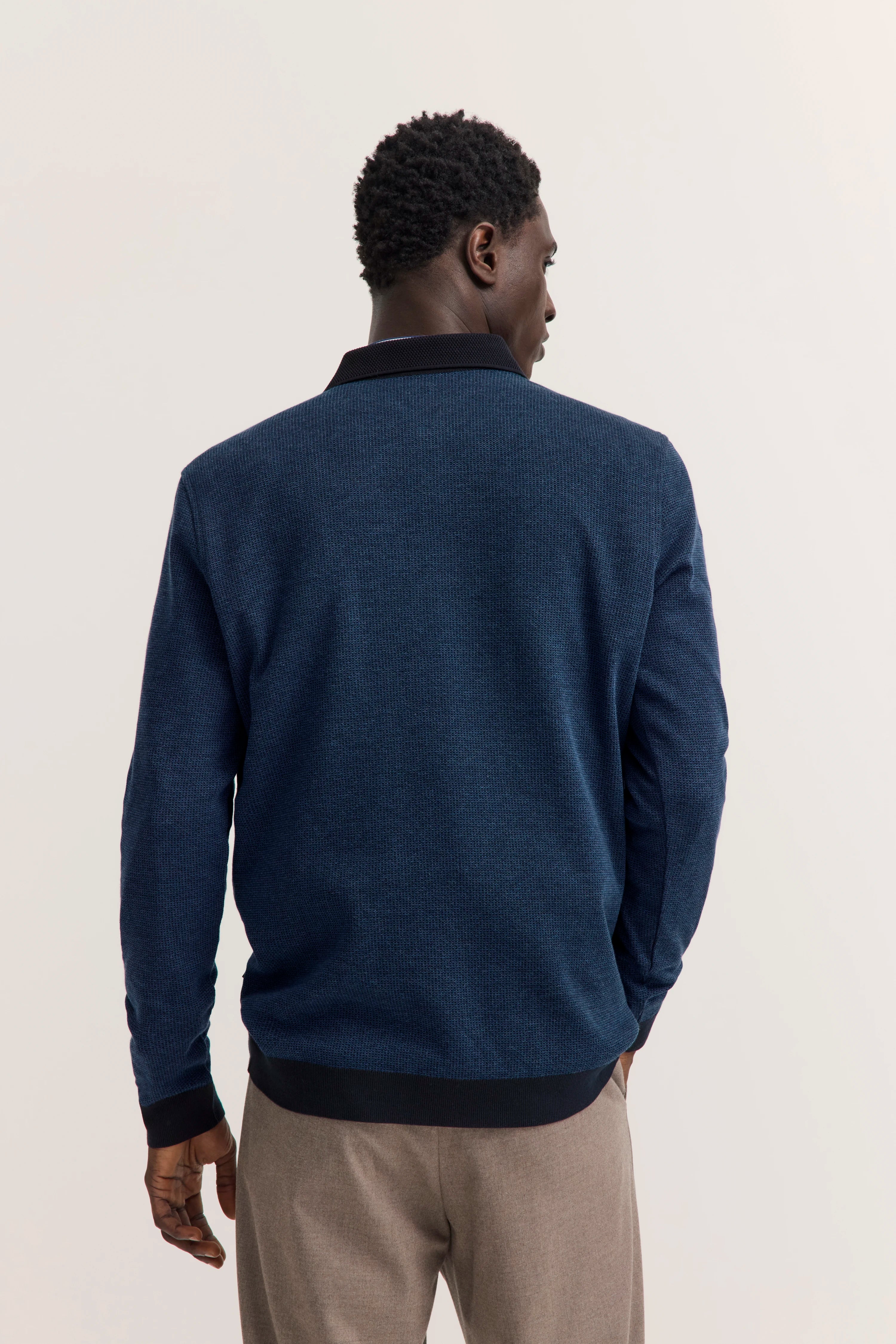 Rückansicht eines Modells im blauen bugatti Pullover, beige Hose, legeres Posing.