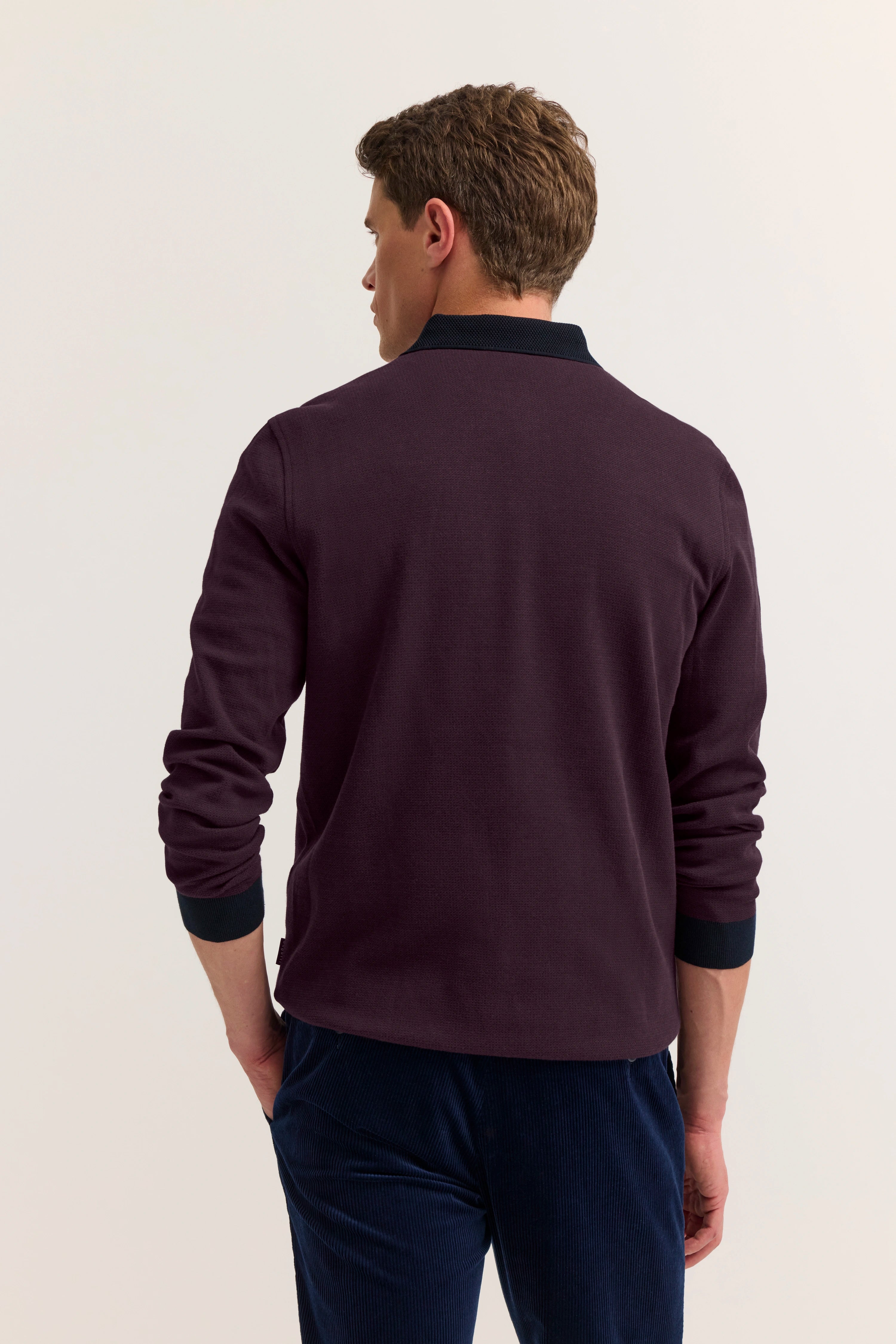Model in burgunderfarbenem Pullover und dunkelblauer Hose von bugatti, Rückansicht, lässiges Posing.