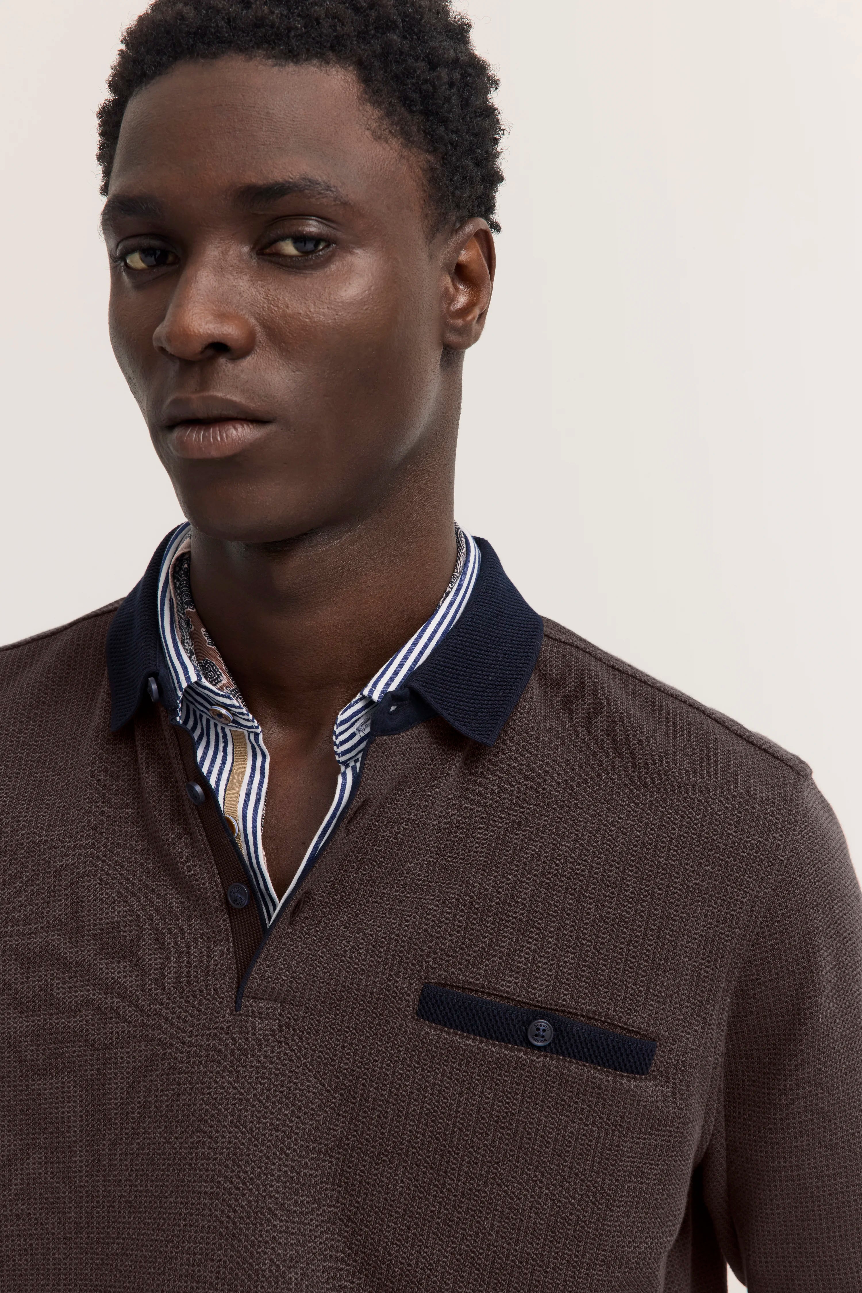 Braunes bugatti-Poloshirt mit blauem Kragen, darunter gestreiftes Hemd. Büstenbild.