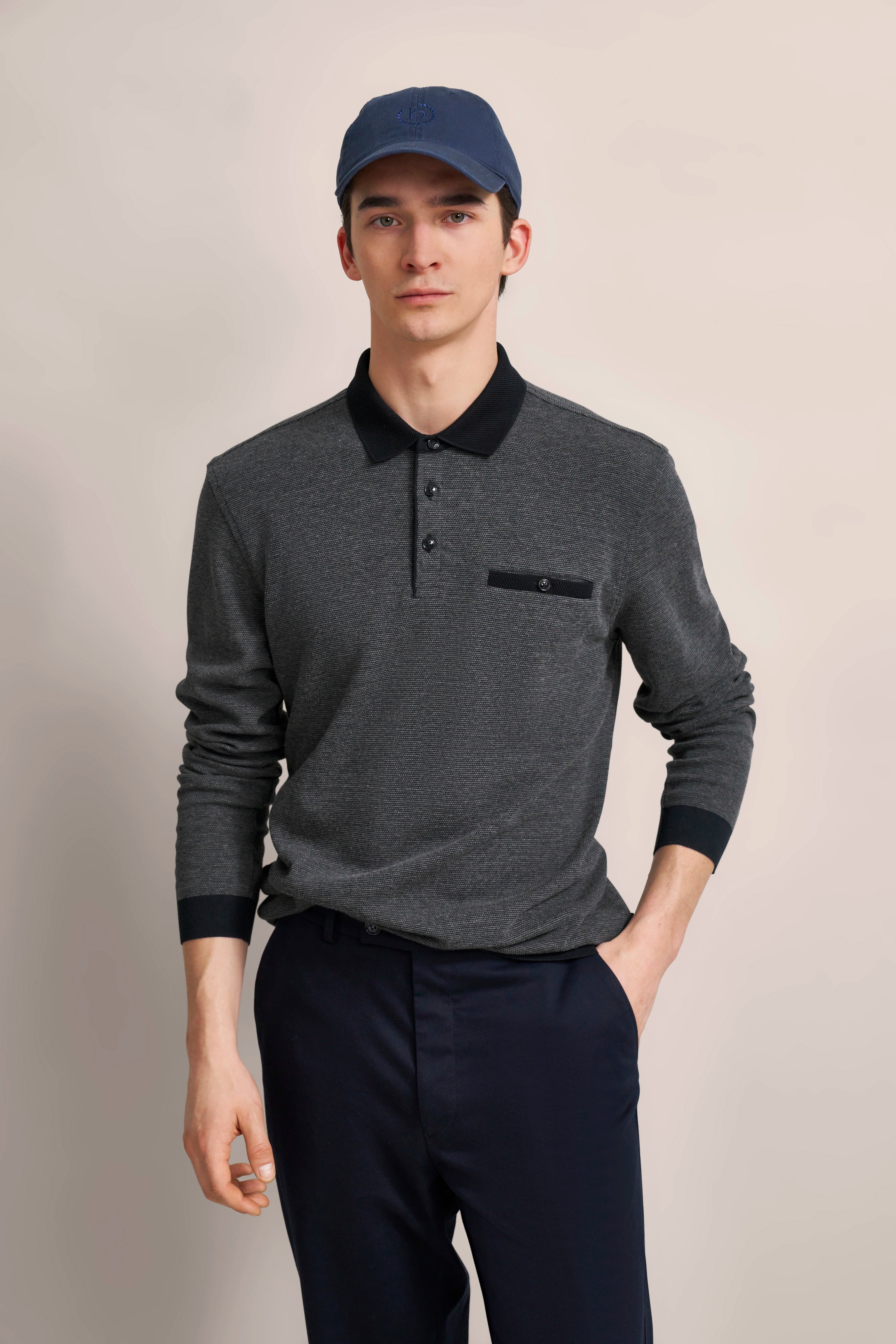 Man in gray polo shirt with black collar and blue pants, exuding relaxed elegance.