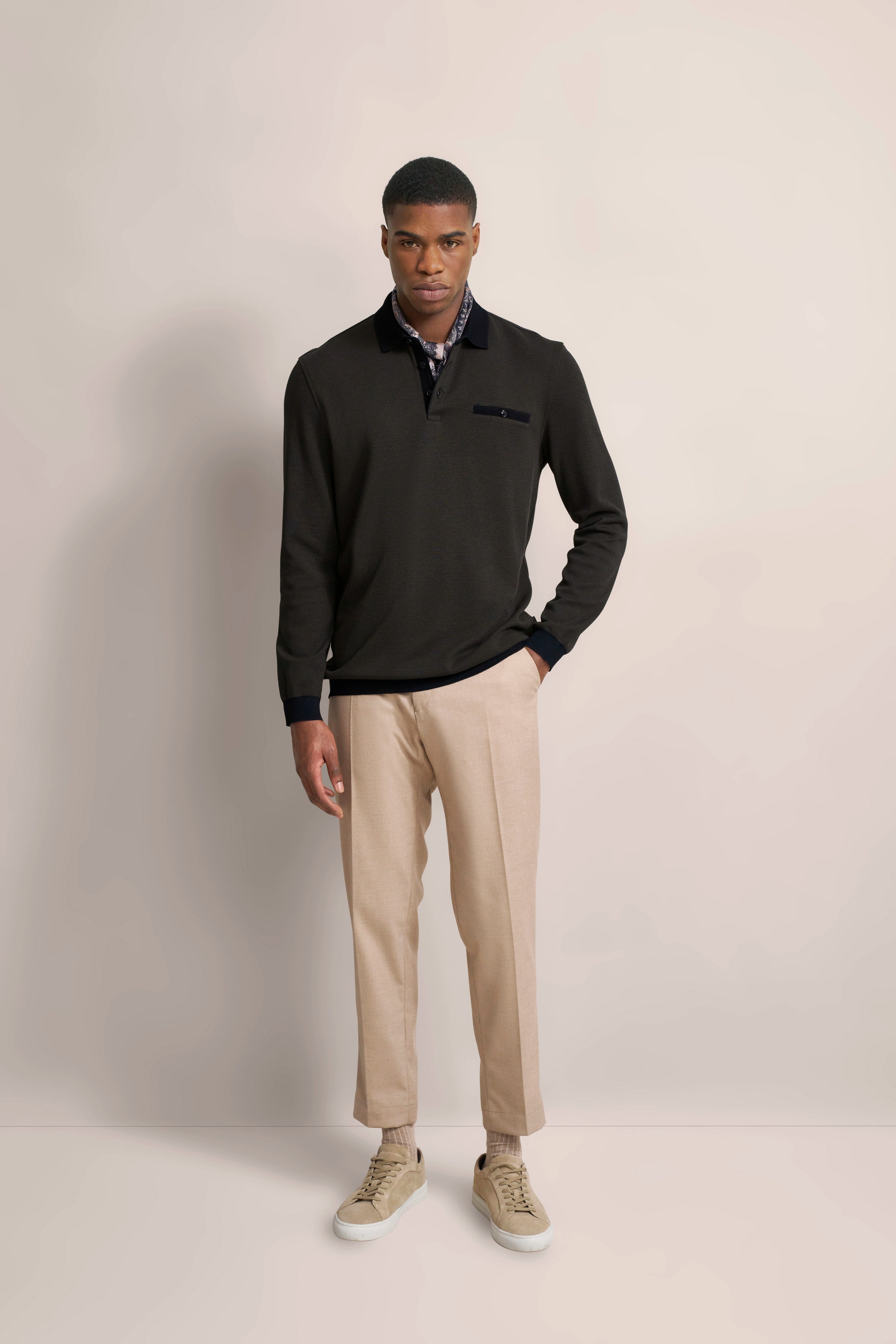 bugatti Modelbild: Schwarzer Pullover, beige Hose, helle Sneaker, lässige Pose.