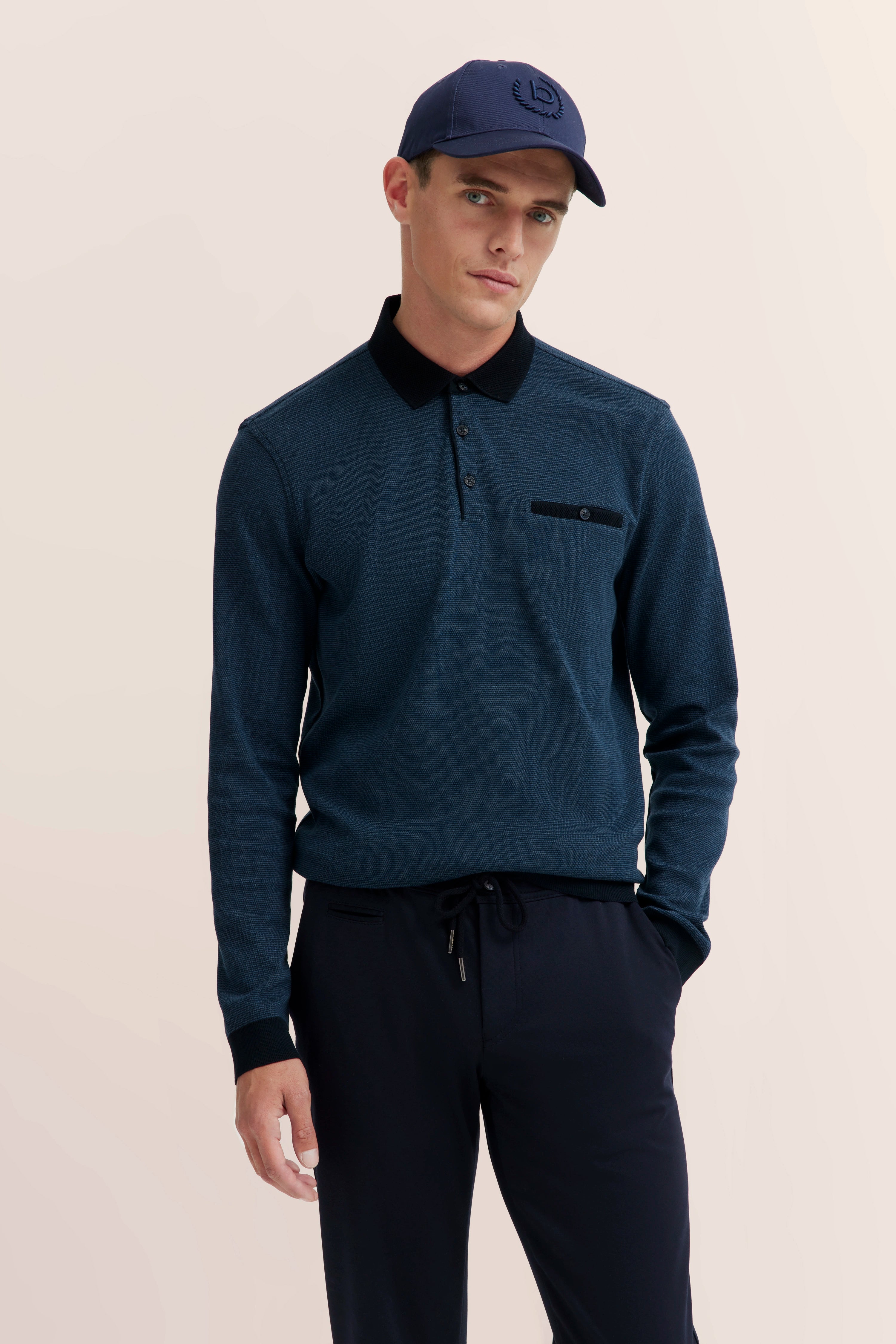 bugatti model: Man in blue polo, black pants, blue cap, standing casually.