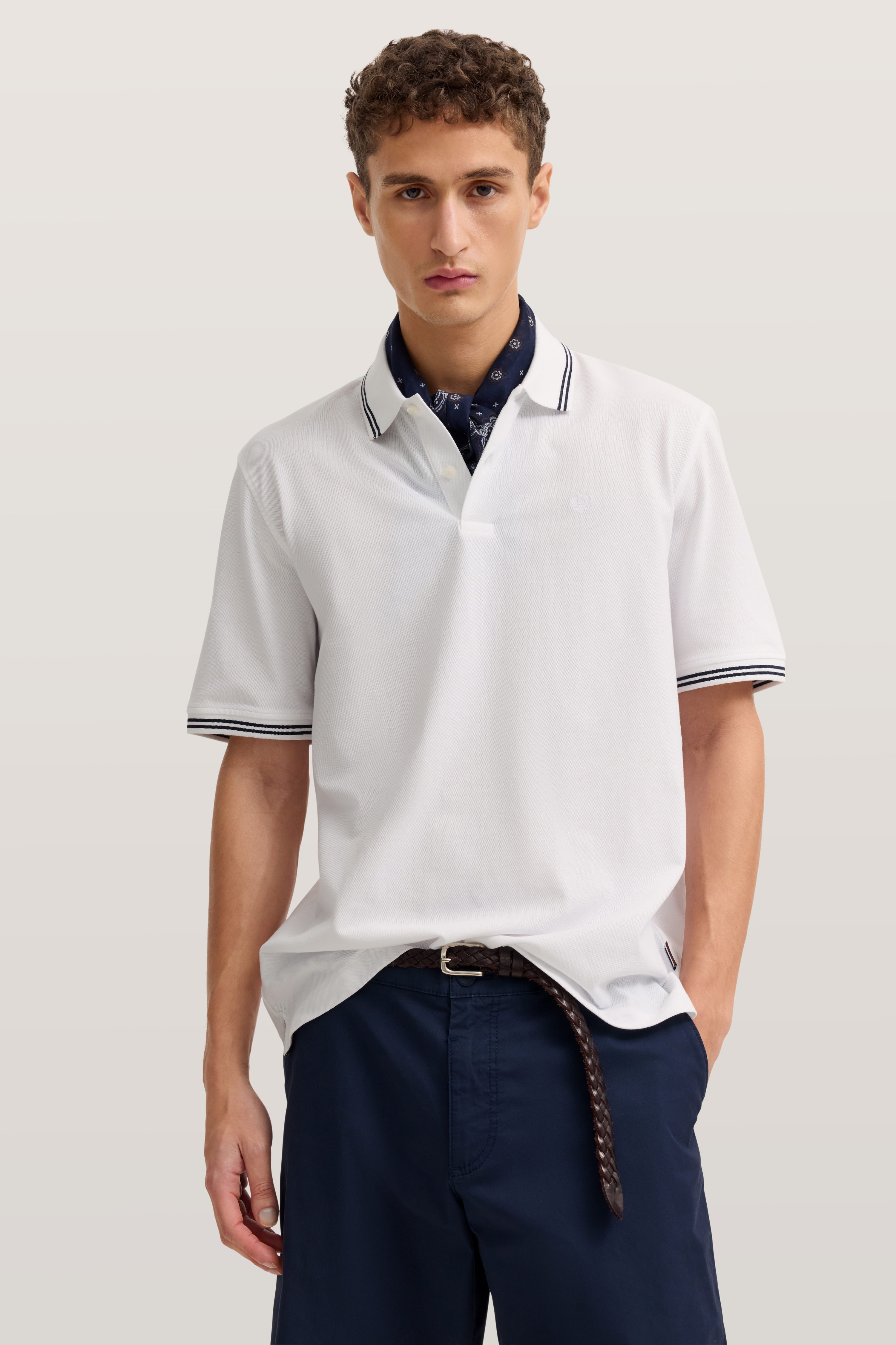 Weißes Polohemd mit Kontrastkragen, marineblaue Shorts, legeres Modelbild, entspannte Haltung.