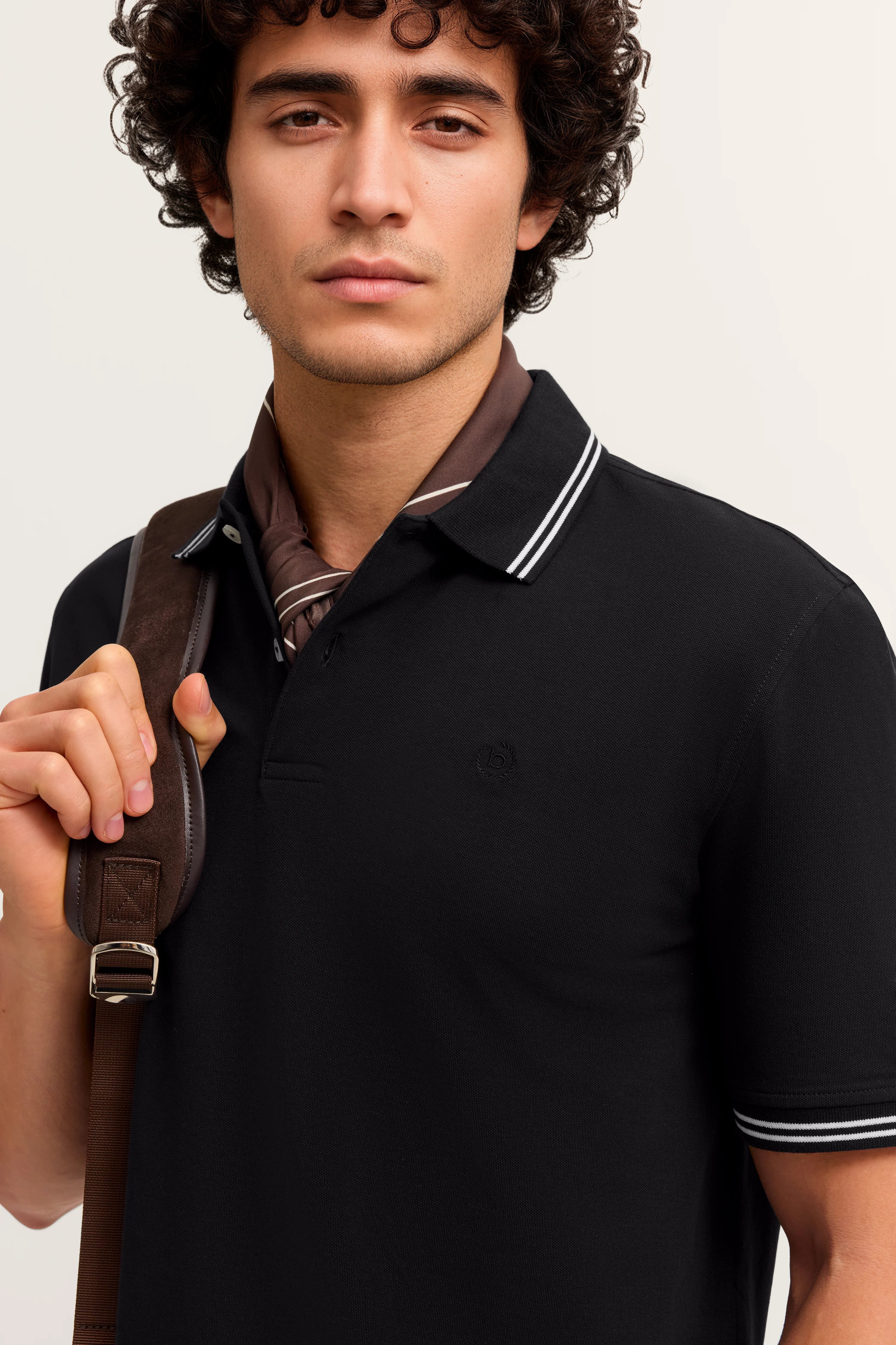 Schwarzes bugatti-Polohemd, braunes Halstuch, legeres Modelbild mit entspannter Pose.