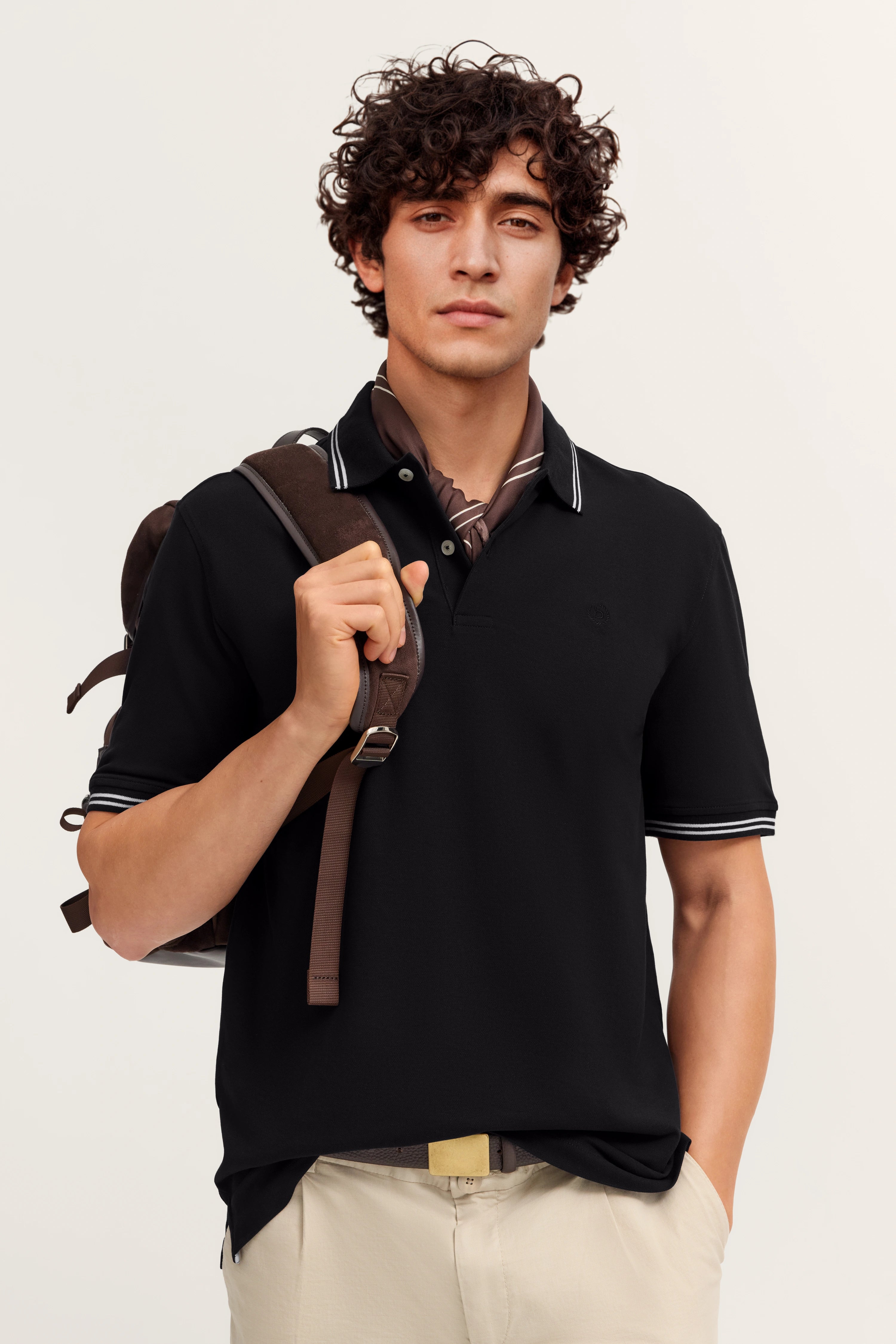 Model trägt schwarzes bugatti Polohemd und beige Hose, legeres Posing mit Rucksack.