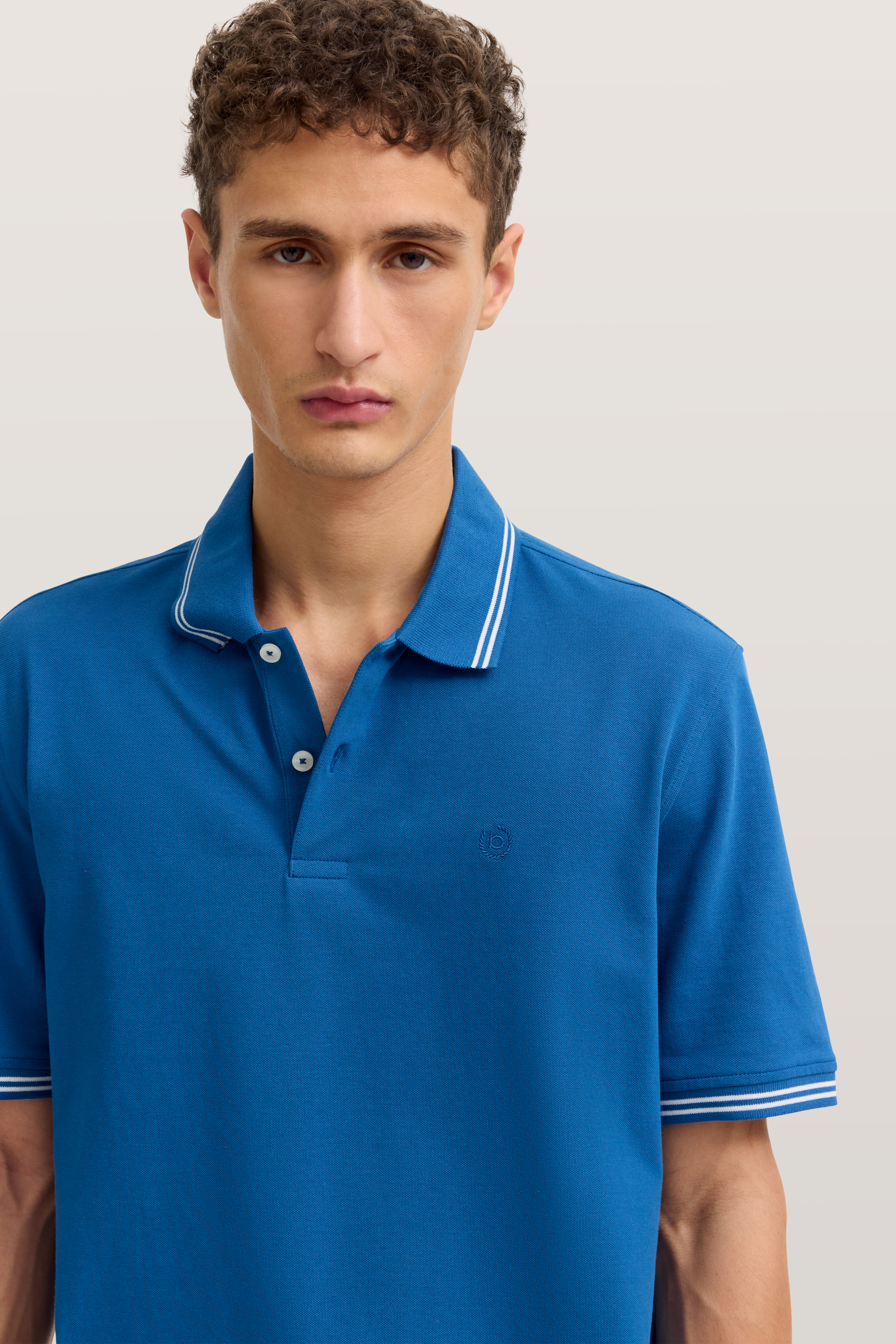 Blaues bugatti Poloshirt, weißer Streifen am Kragen, Modelbild, entspannter Gesichtsausdruck.