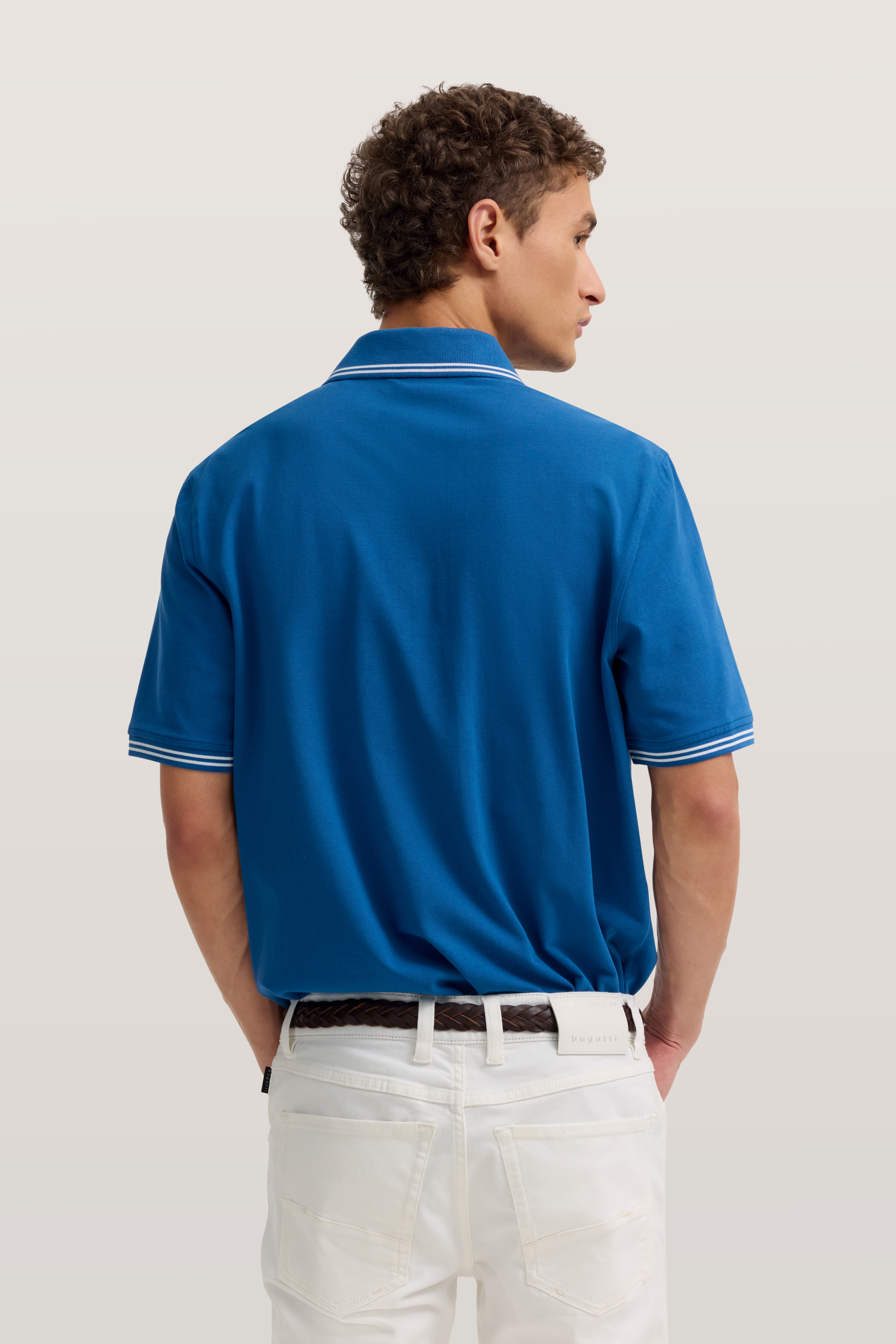 Blaues Polohemd von bugatti, getragen von hinten, kombiniert mit weißen Jeans, legeres Modelbild.