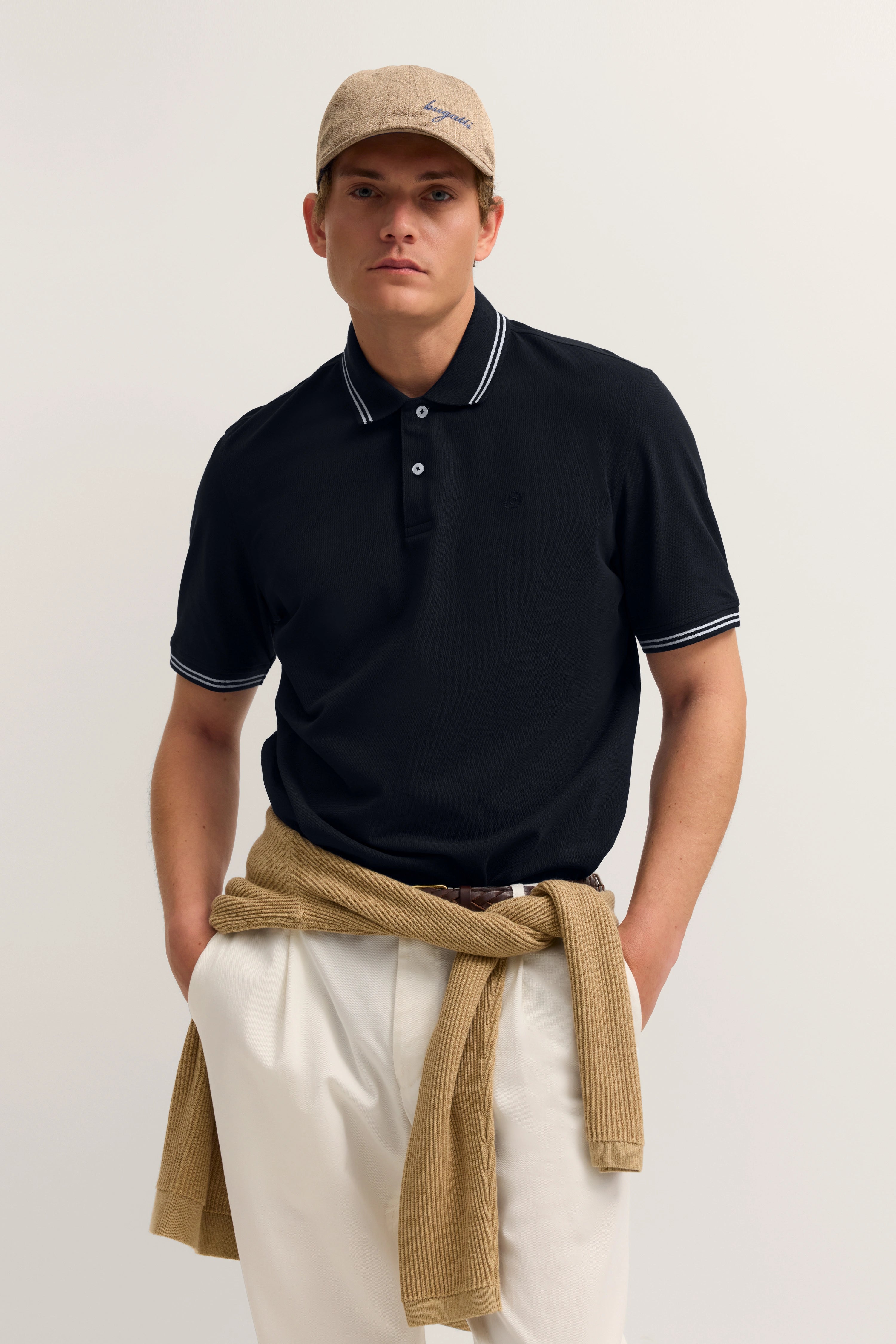 Model in schwarzem Polohemd und beige Hose, Pullover um Taille gebunden, bugatti-Kappe.