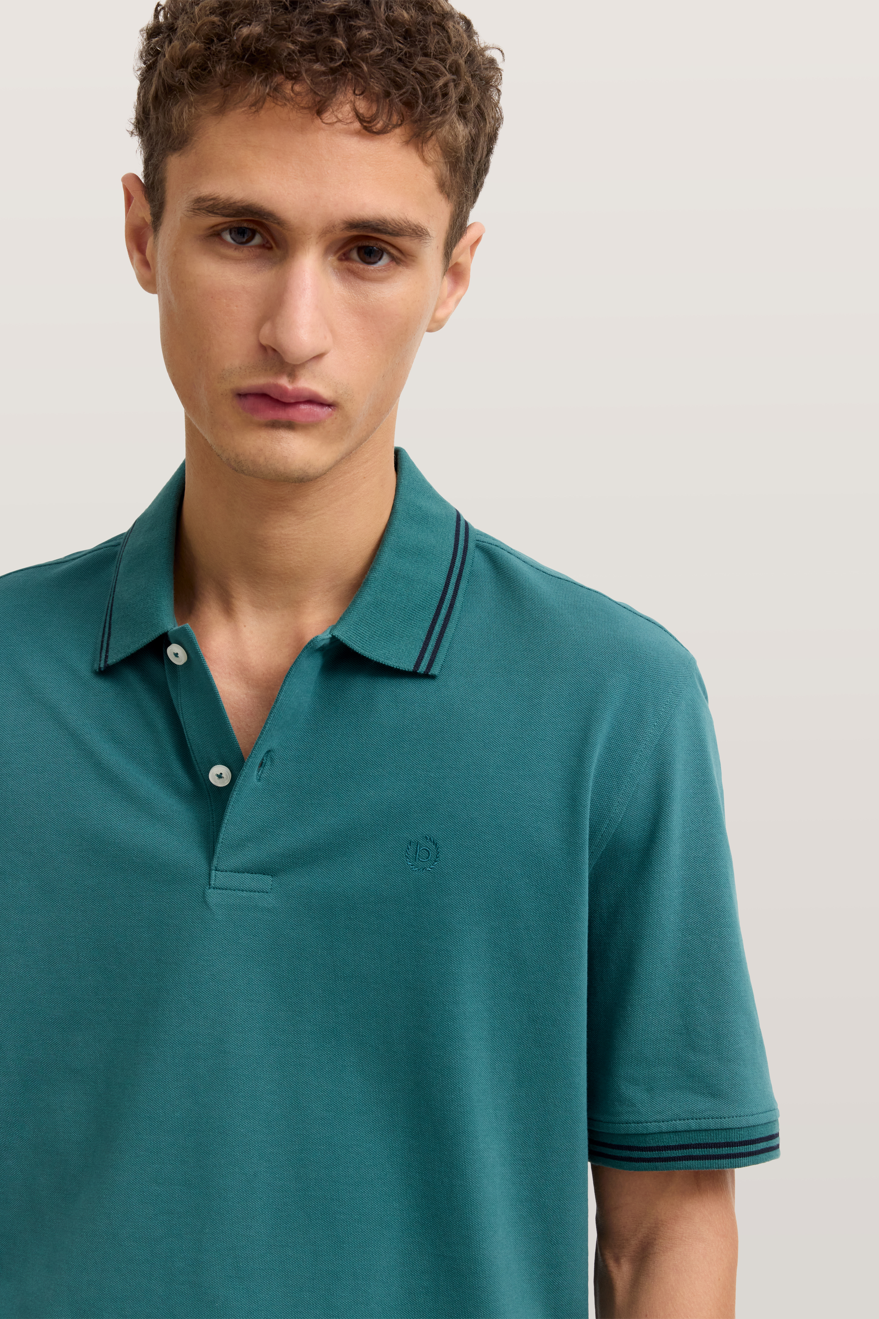 Model in petrolfarbenem bugatti Polohemd mit feinen Streifen, legerer Look.