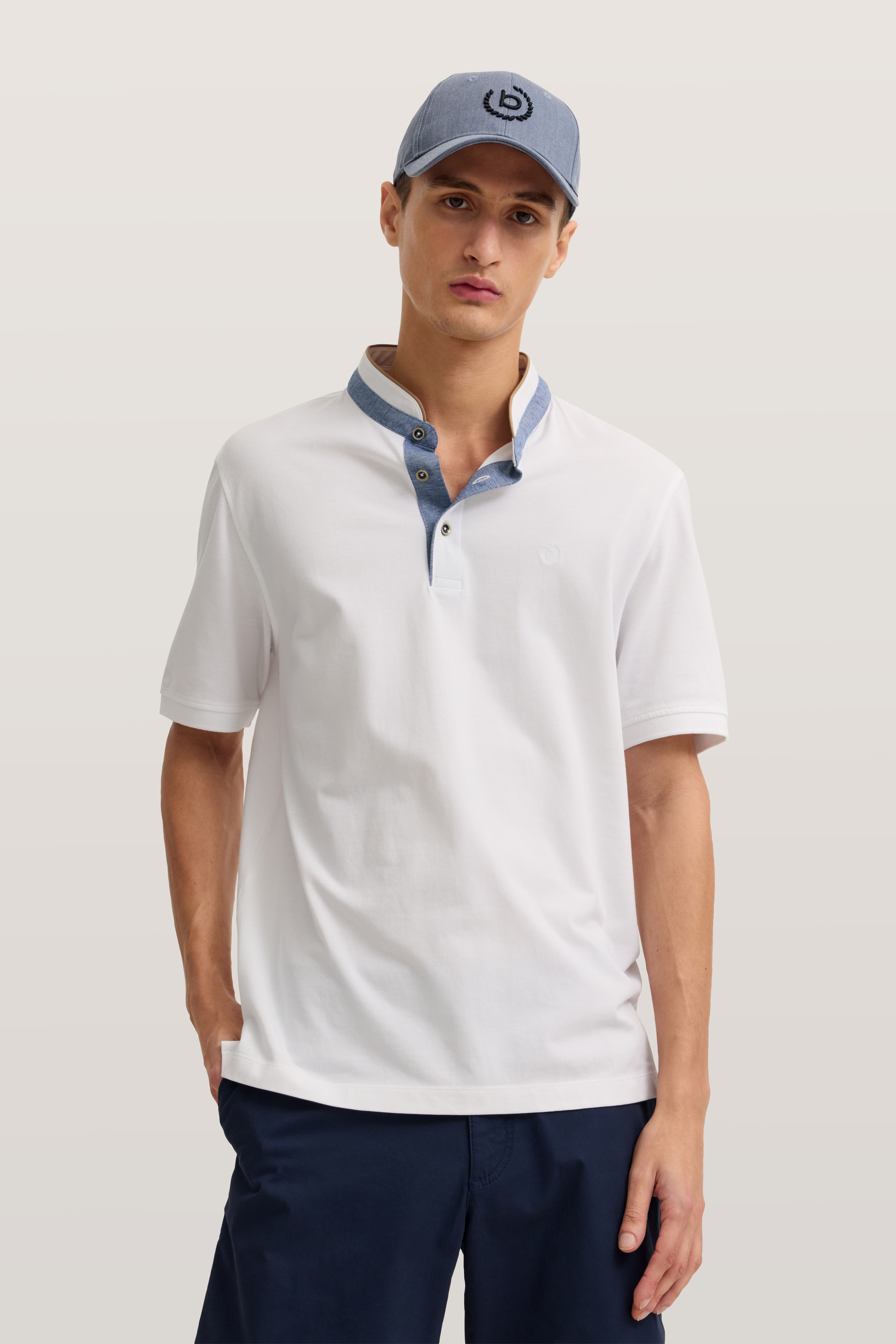 Weißes Polo mit blauem Kragen, blaue Shorts, blaues Cap, Modelbild mit entspanntem Stand.