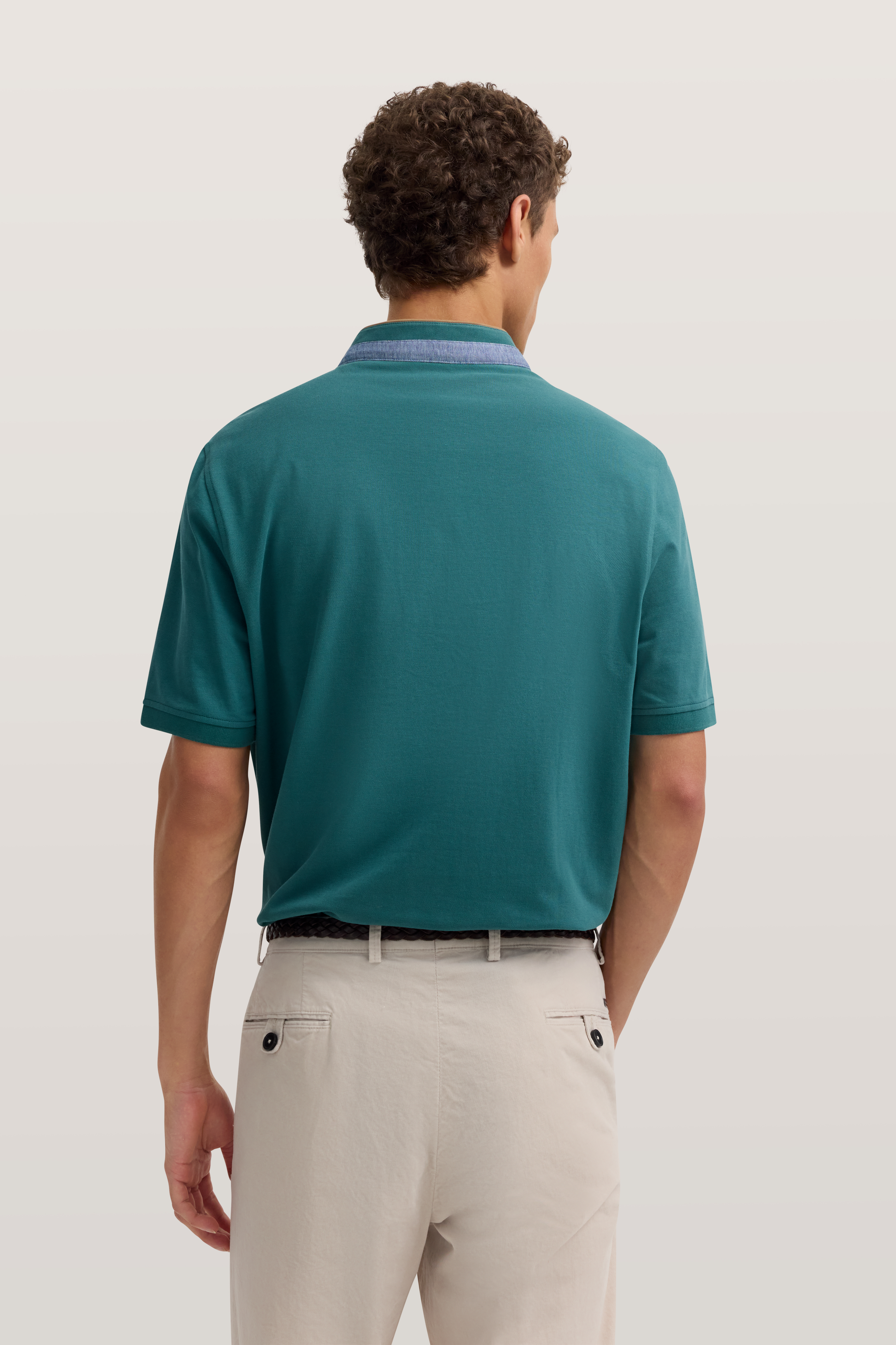 Hinteransicht Model in türkisfarbenem Poloshirt und beigen Hosen, legeres Posing.