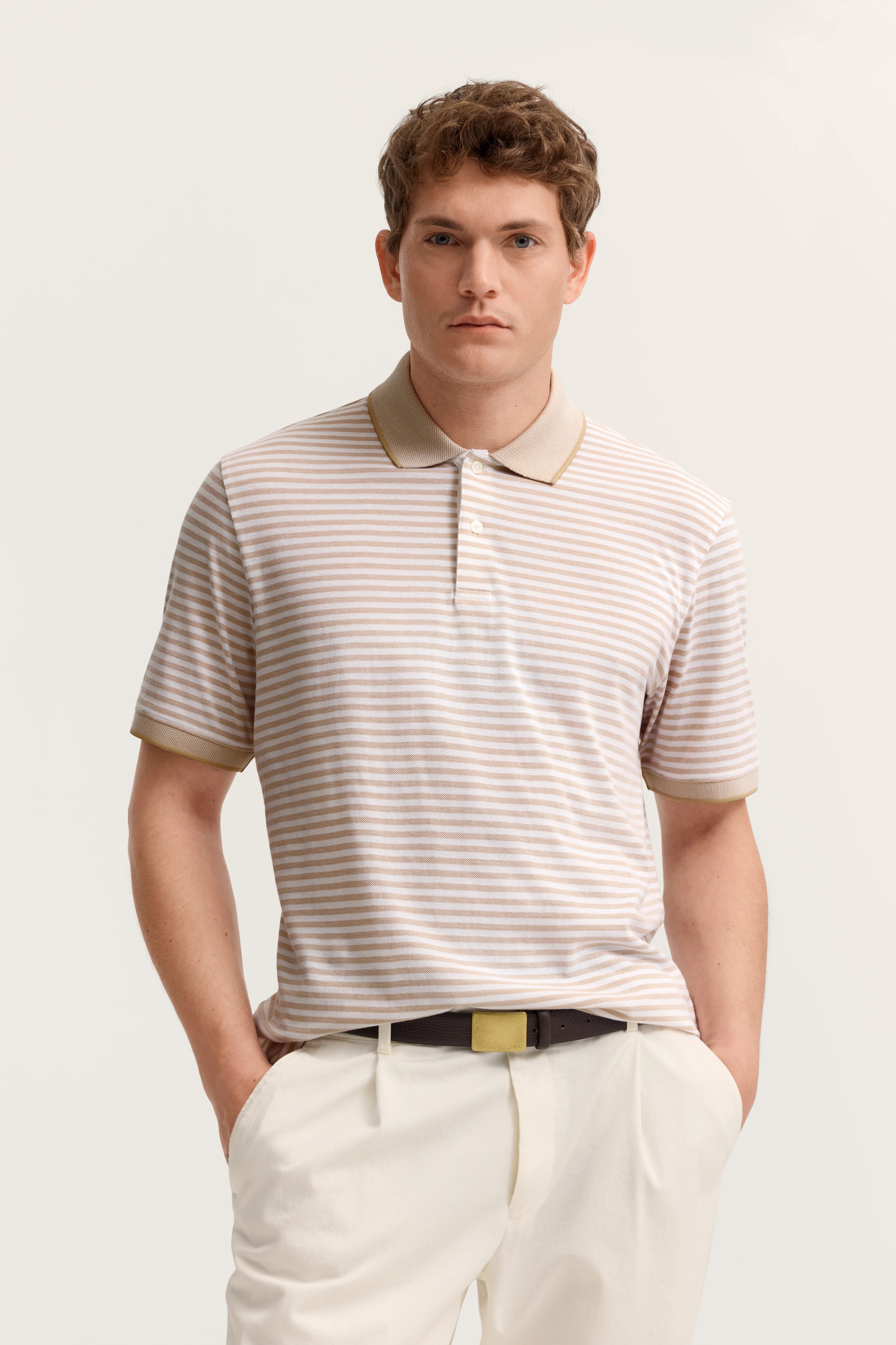 Das Model trägt ein gestreiftes Poloshirt in Beige und Weiß, kombiniert mit weißen Hosen.