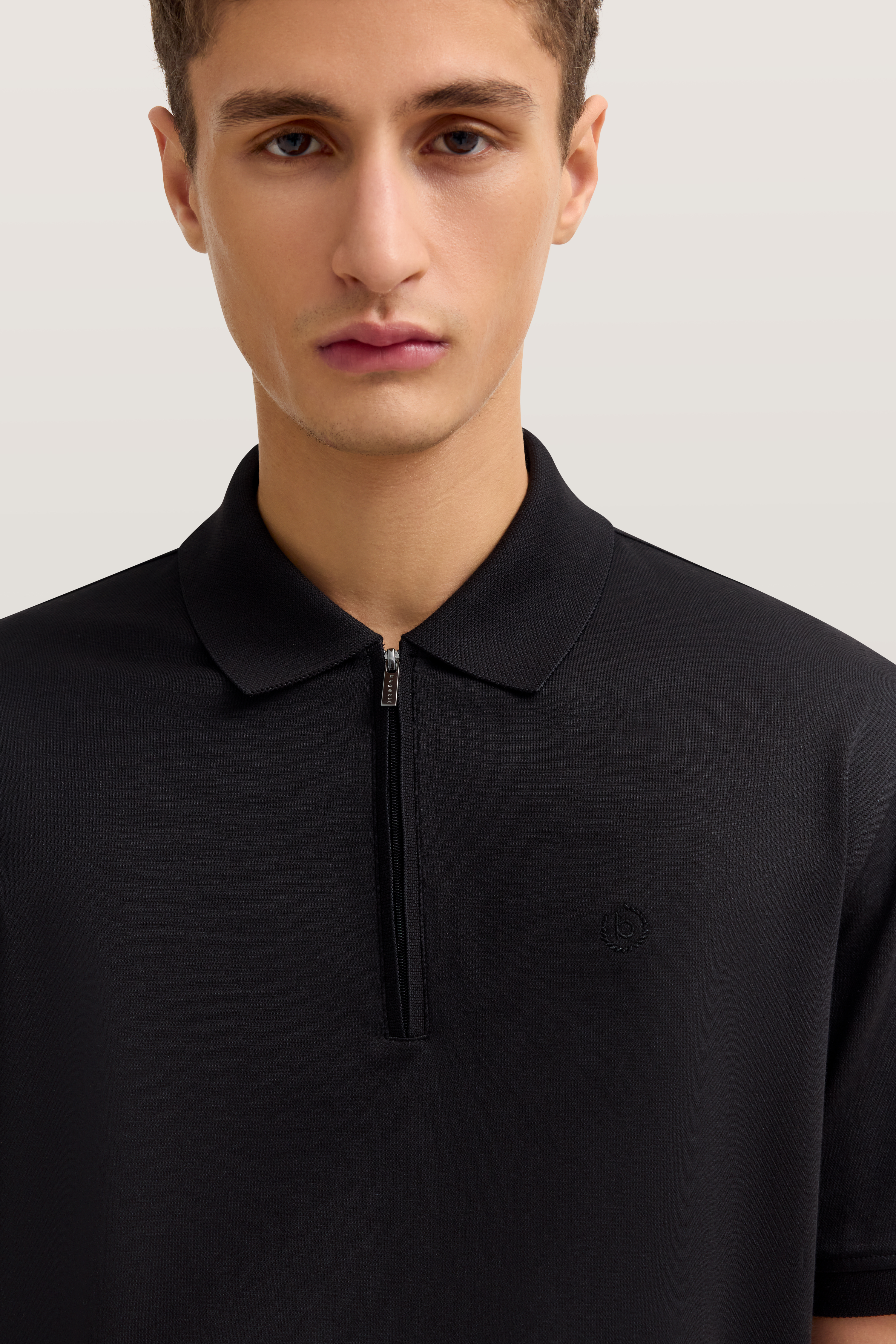 Schwarzes bugatti Polo-Shirt, Nahaufnahme, schlichter Stil, Reißverschluss, dezentes Logo, elegantes Design.