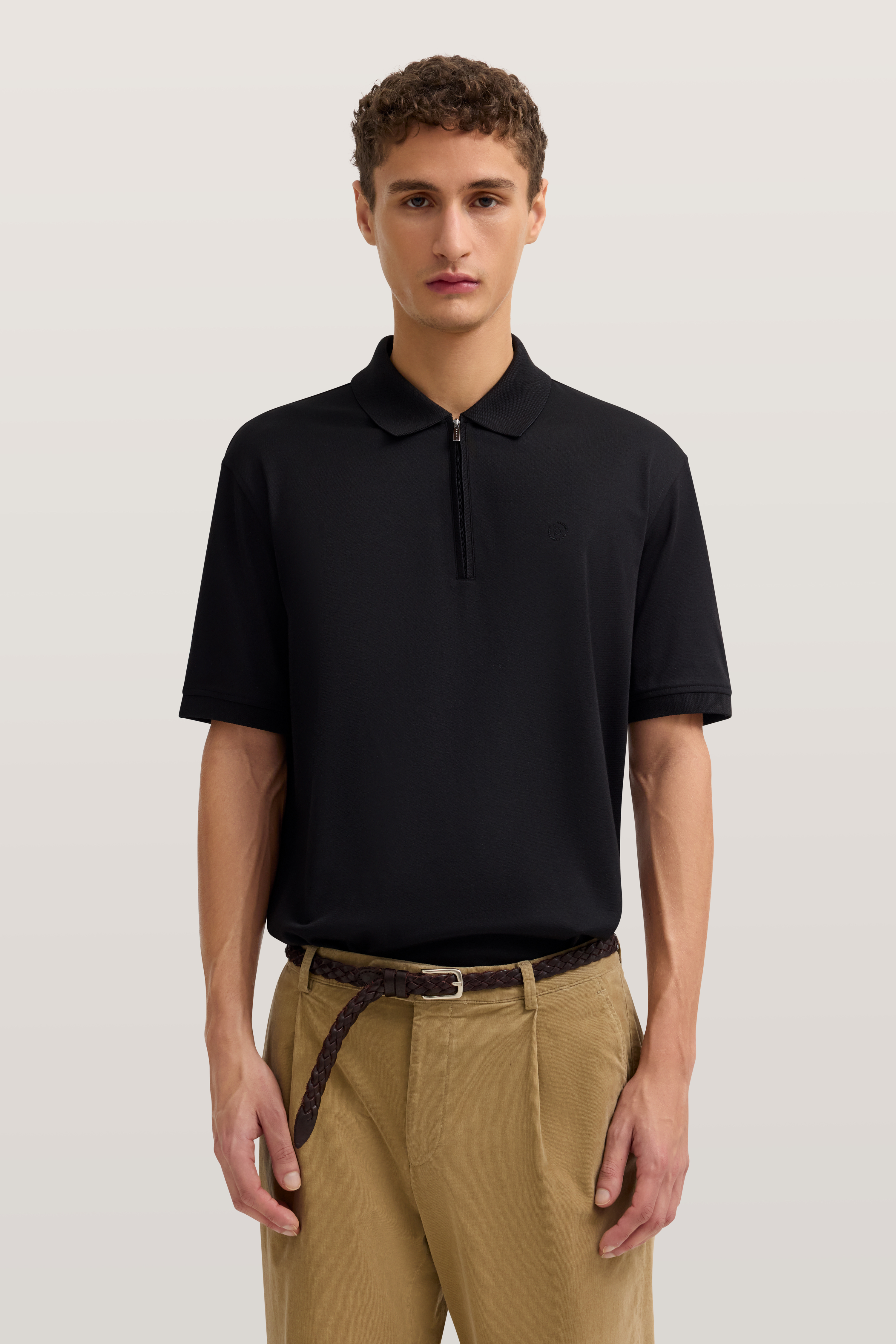 Schwarzes bugatti Polohemd, beige Hose, Model stehend, entspannte Haltung.