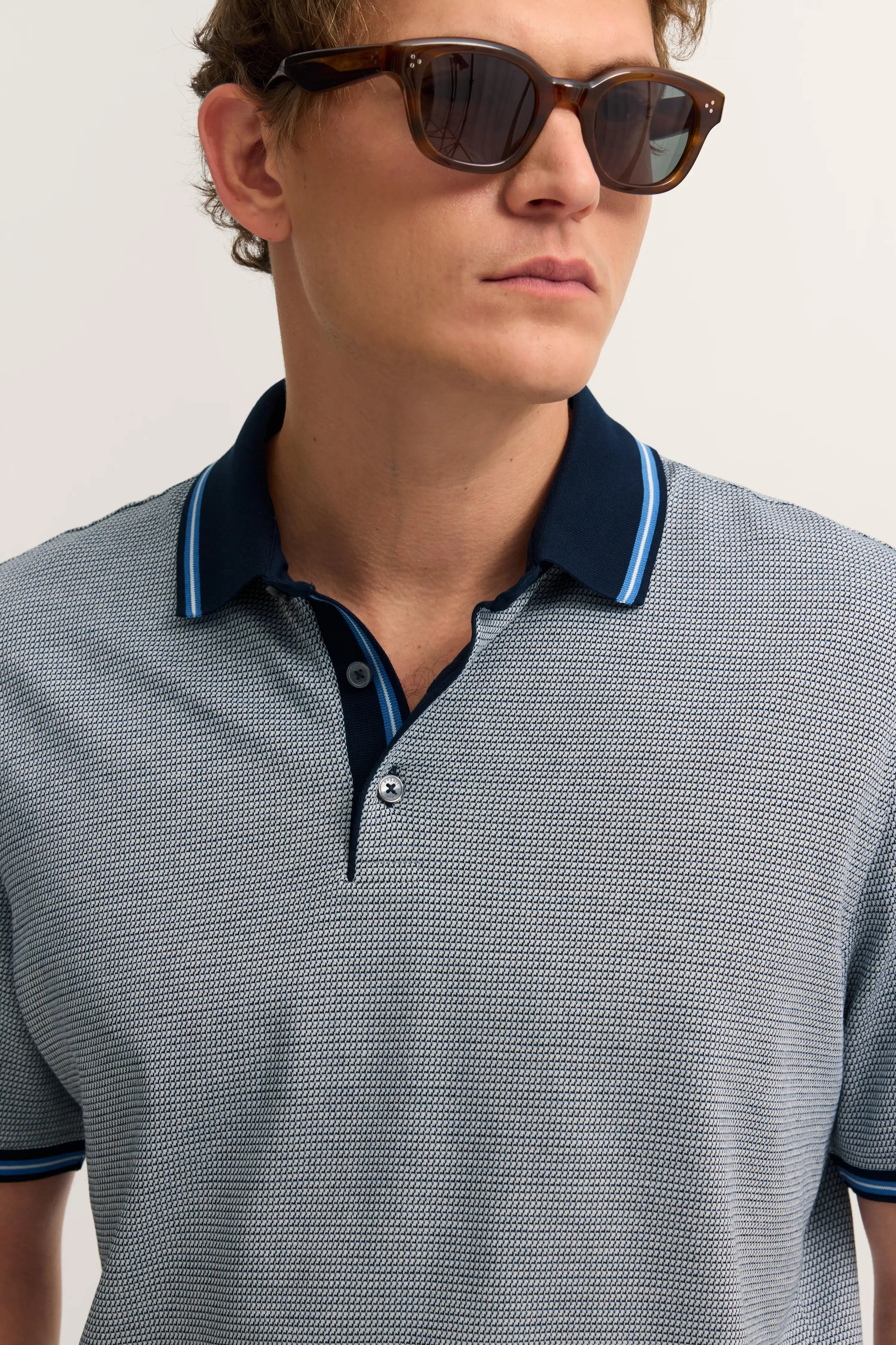 bugatti Polohemd in Grau-Blau mit feinem Muster, Modelbild, lässige Pose, Sonnenbrille.