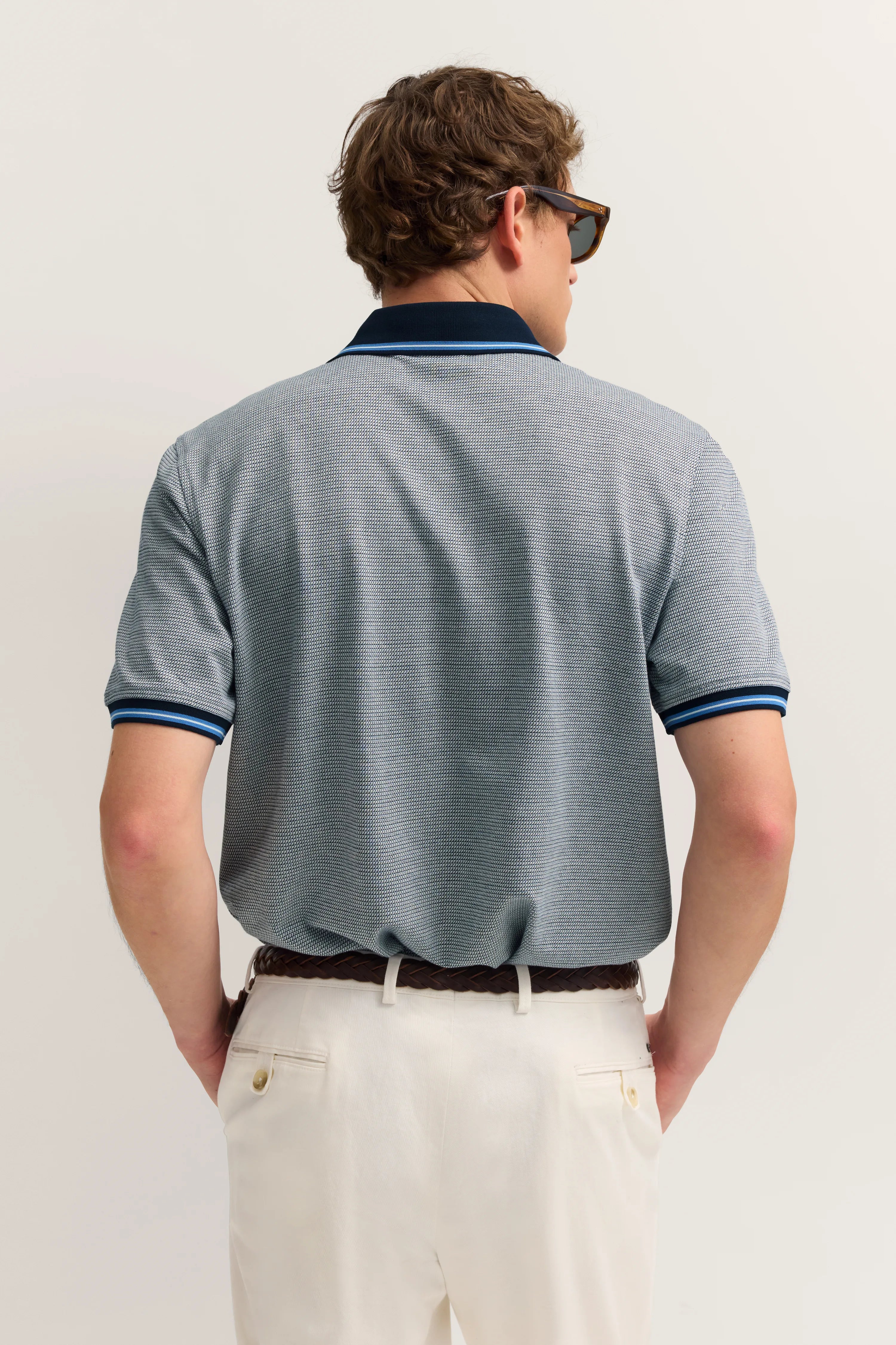 Bugatti Polo in Grau mit blauen Akzenten, weißer Hose, Model von hinten, lässige Pose.