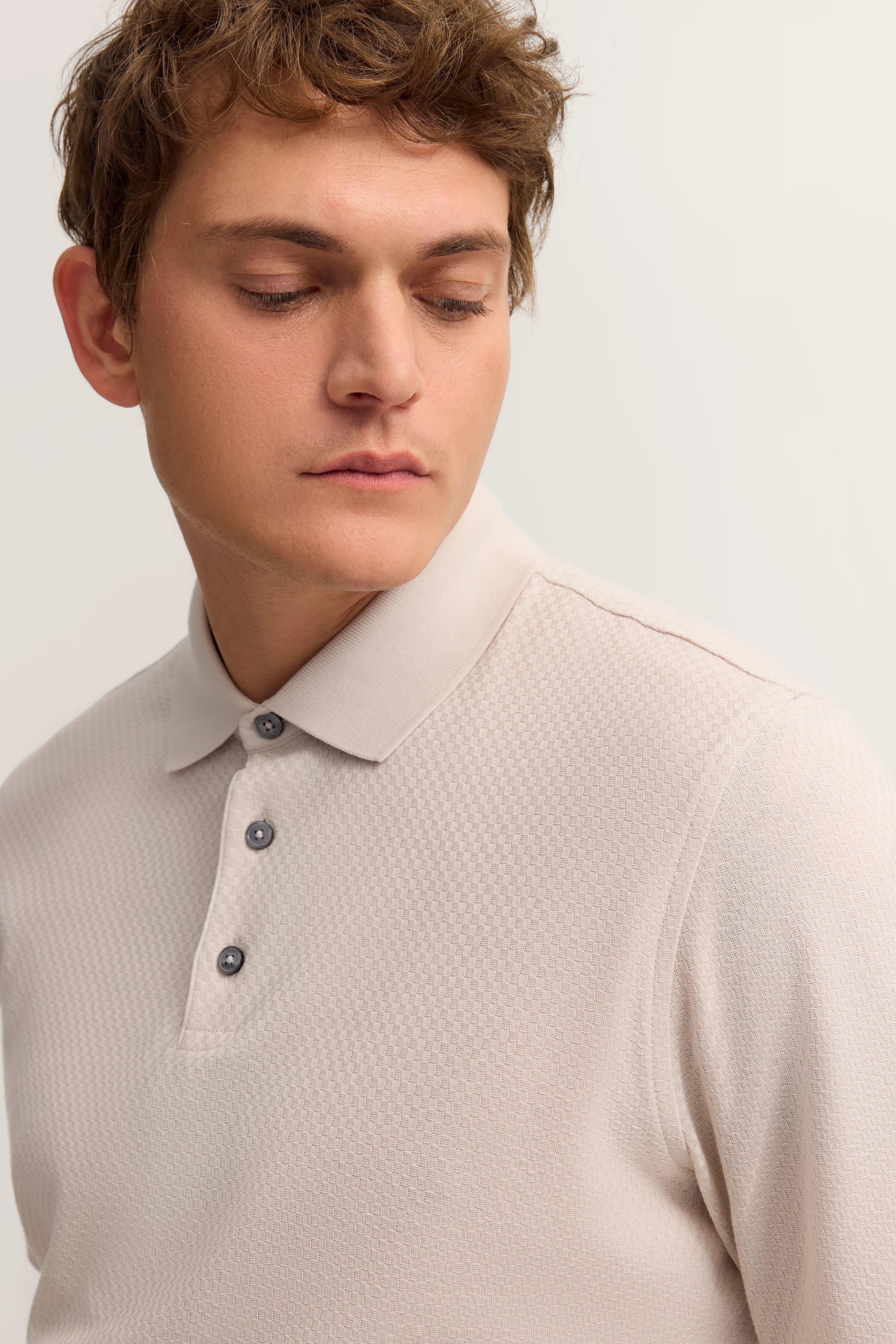 Beiges Polo-Shirt mit dezentem Muster, getragen von Model in entspanntem, nachdenklichem Posing.