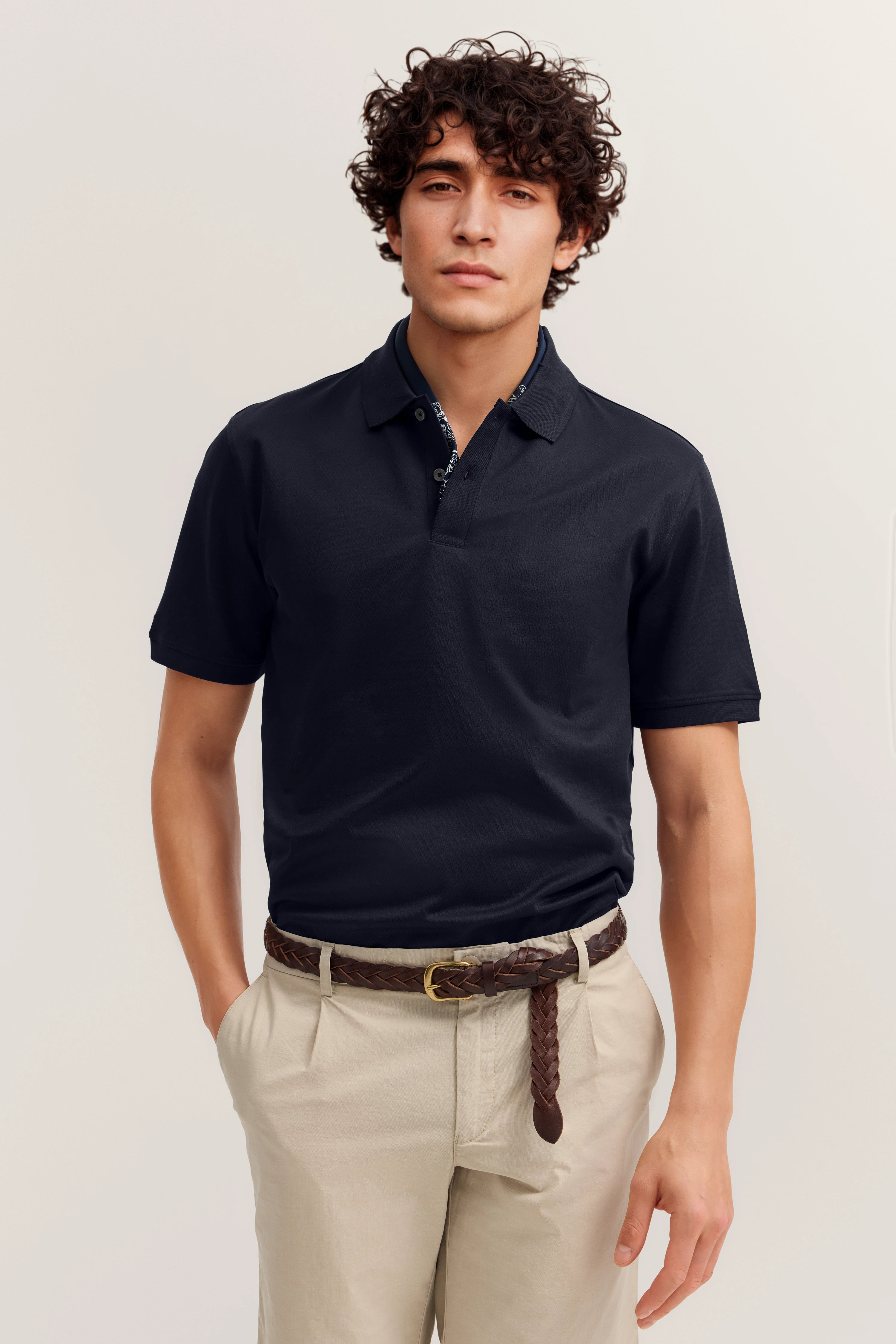 Bugatti Model in dunkelblauem Polo, beiger Hose, lässige Pose, Hände in Hosentaschen.