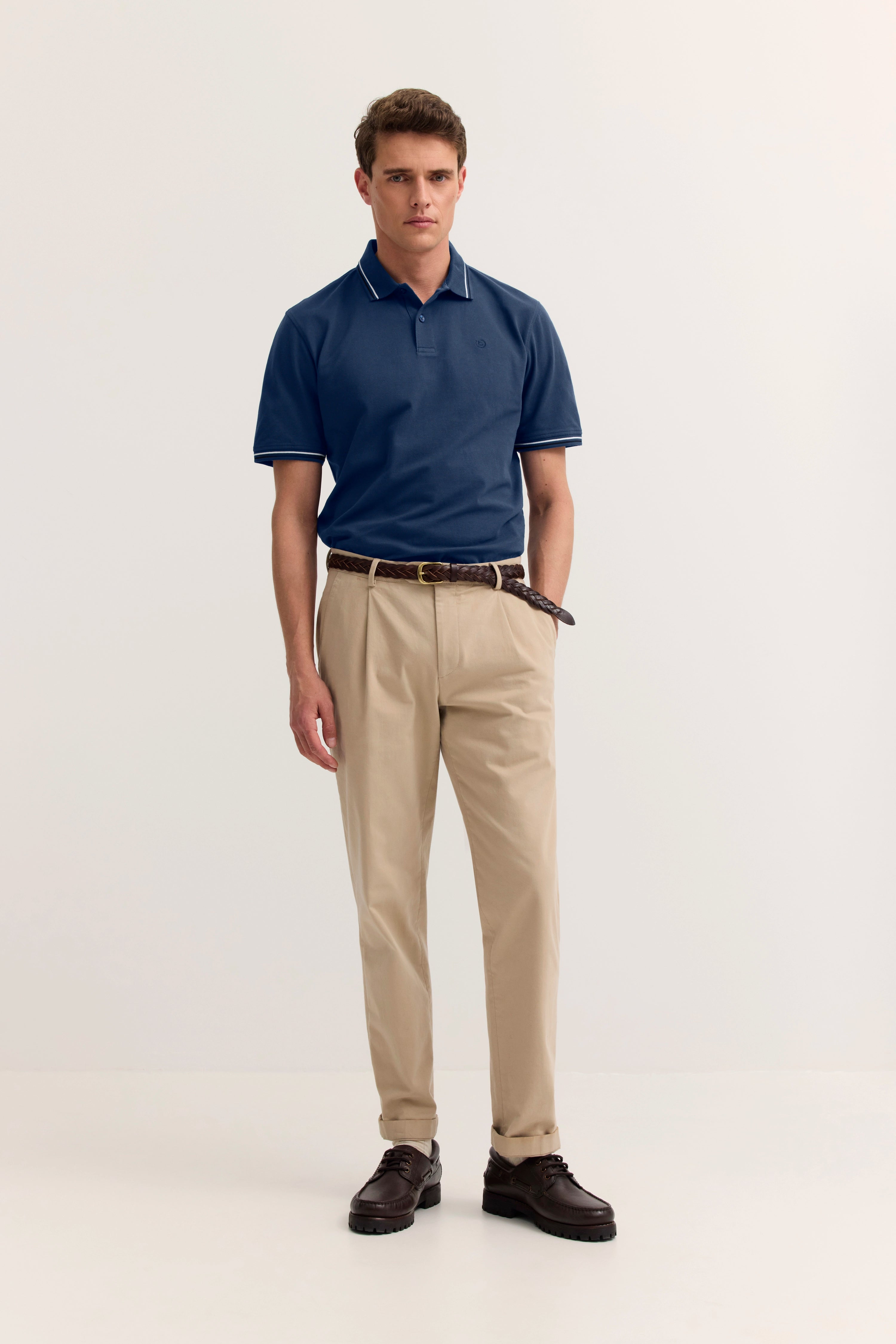 Model in blauer Poloshirt von bugatti, beige Chinos, brauner Gürtel, braune Schuhe, entspanntes Posing.