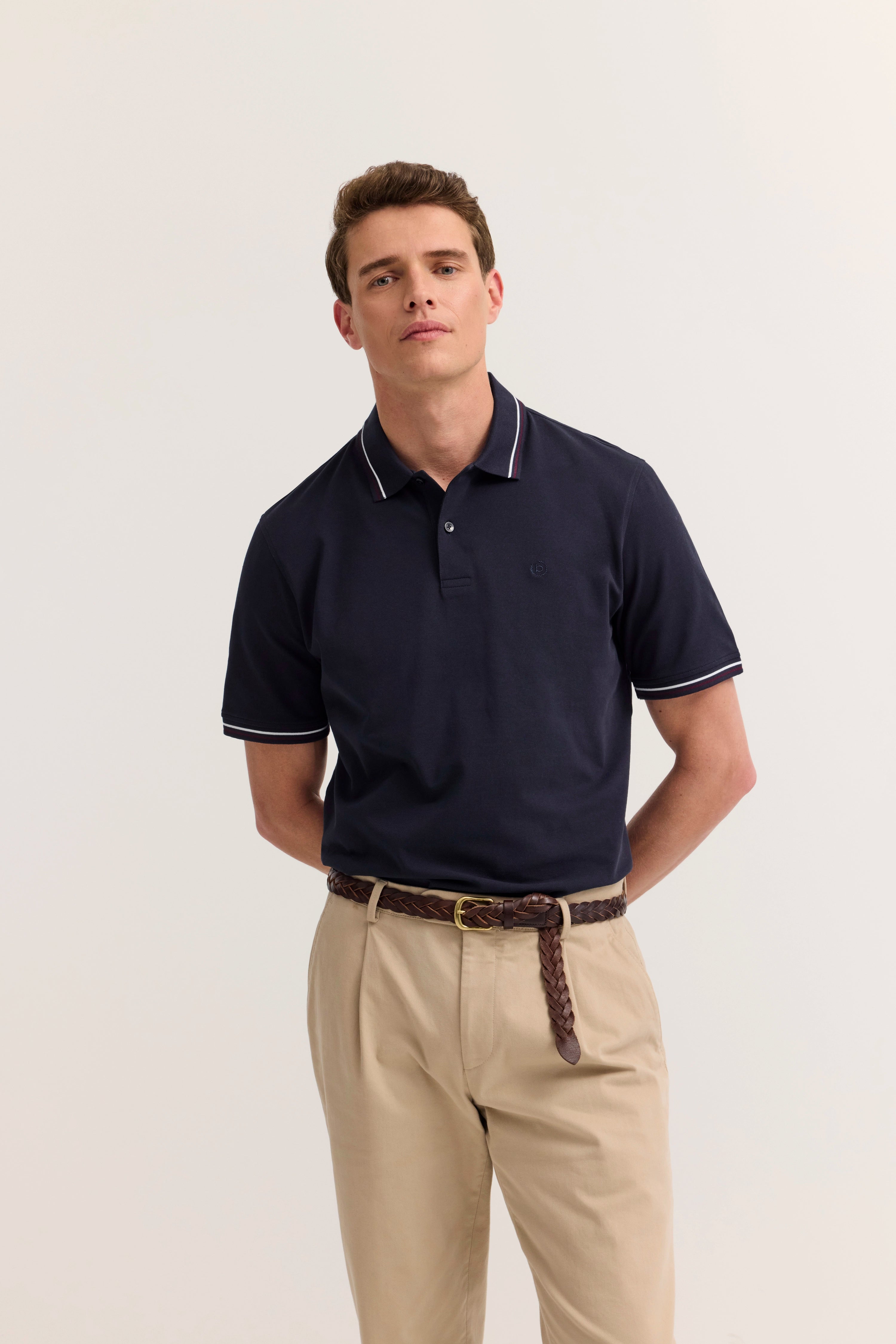Navy Polo und beige Chinos, Model posiert mit entspanntem Ausdruck, bugatti Stil.