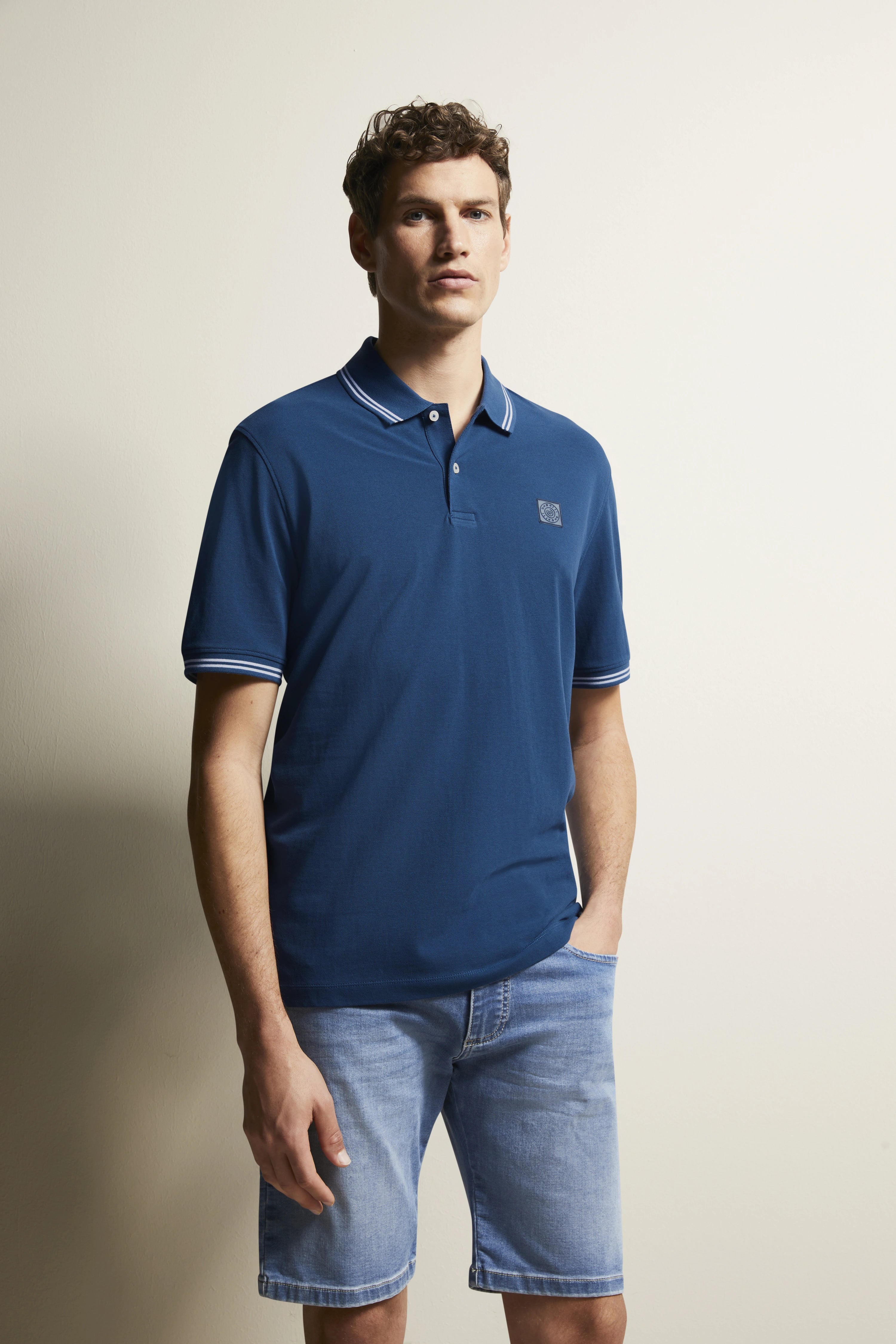 Blue polo and denim shorts, casual model image, hands in pockets, relaxed style by bugatti.