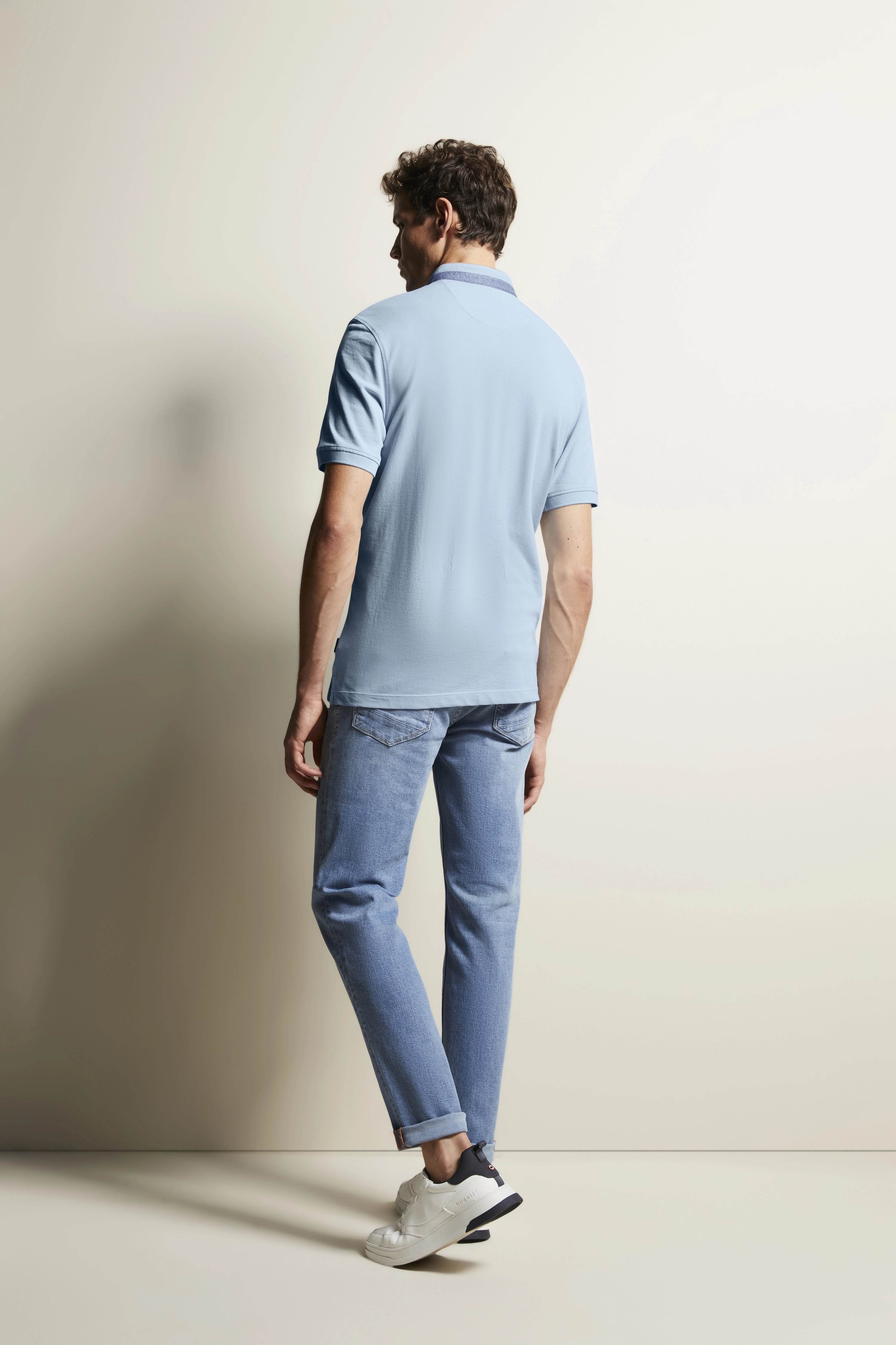 Model in hellblauem Polo und Jeans, rückseitige Pose, lässig. bugatti Stil und Raffinesse.