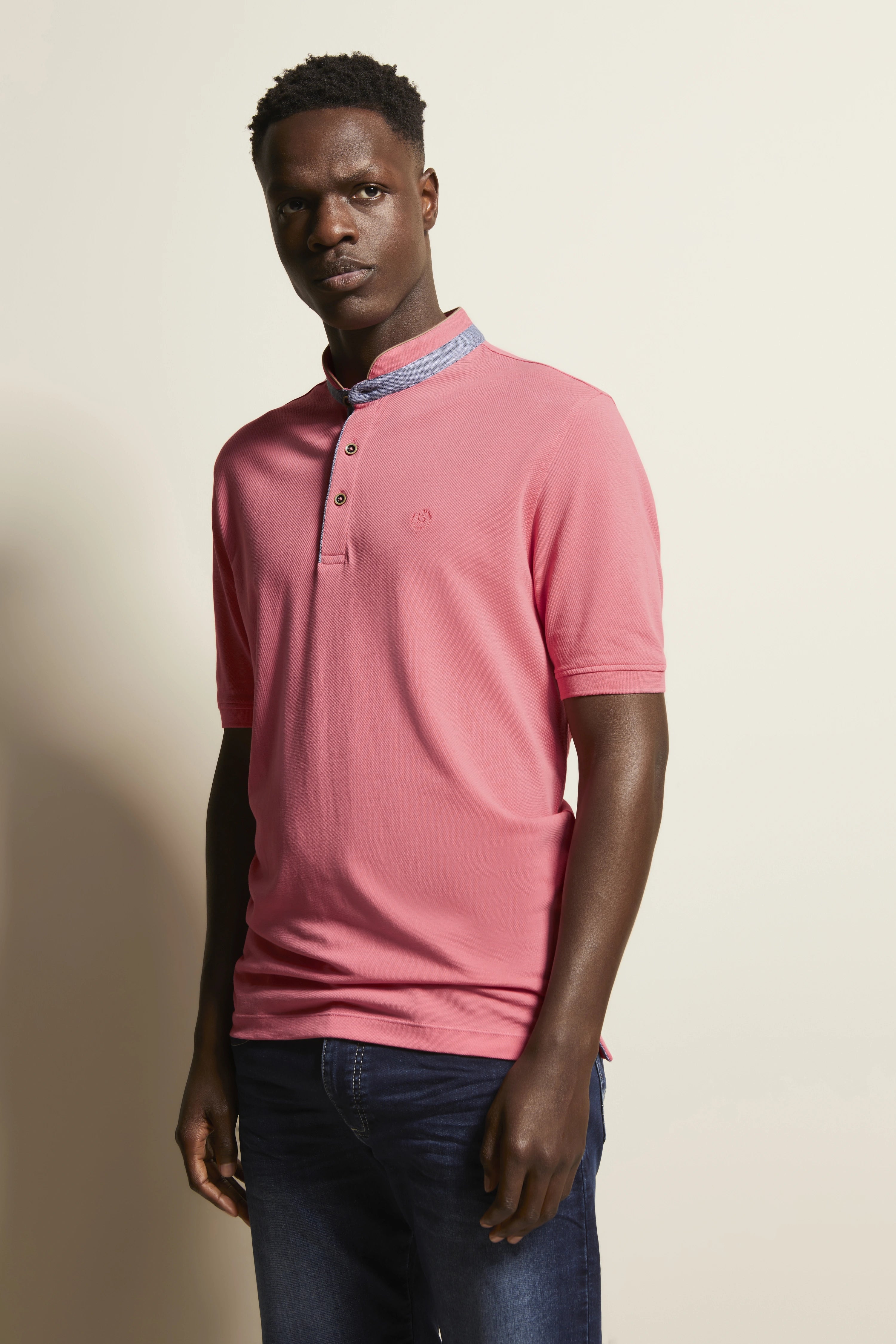 Model: Man draagt roze bugatti polo, blauwe jeans, ontspannen houding, stijl en elegantie.