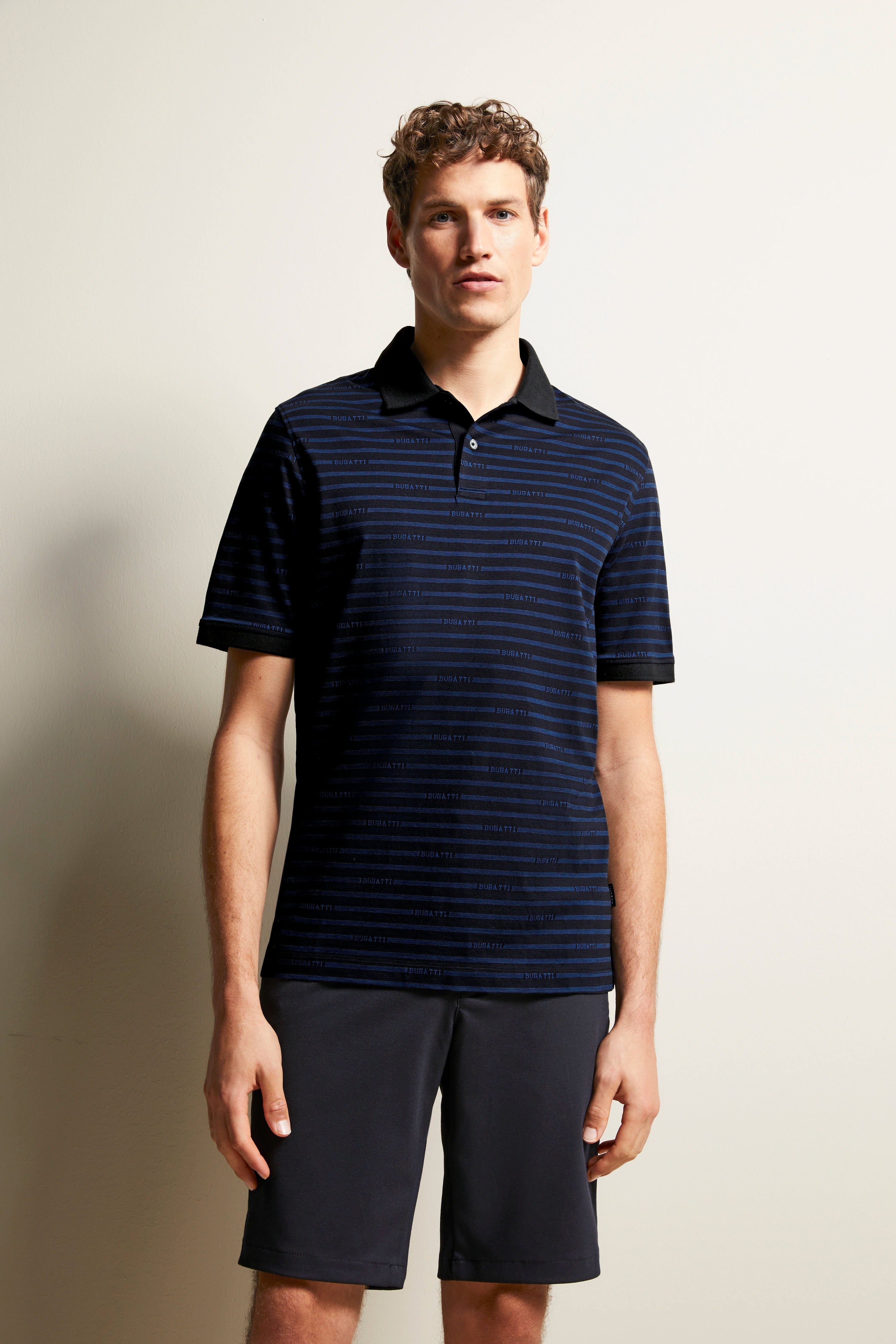 Model in bugatti blue-black striped polo shirt, casually standing with dark shorts.