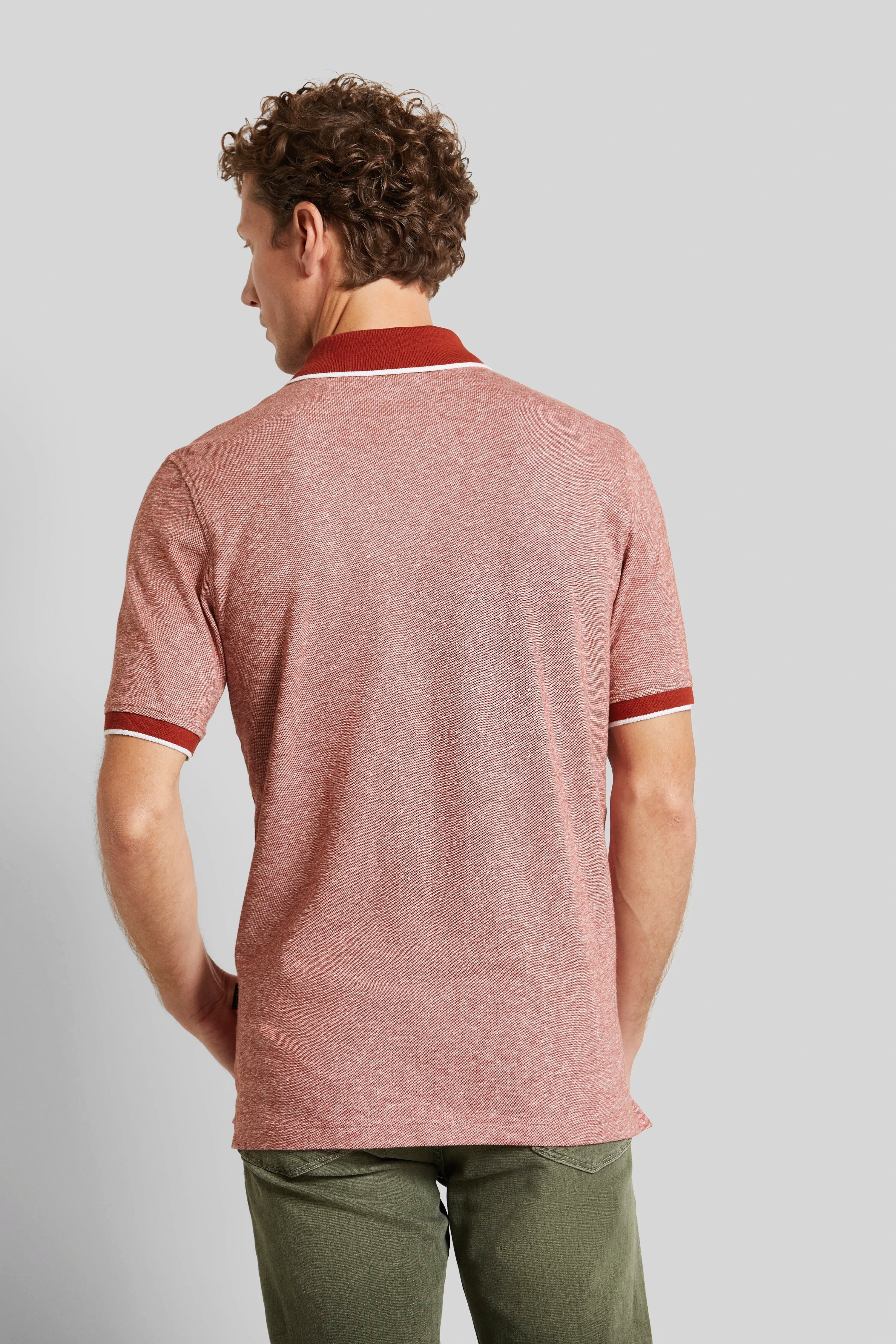 Rückansicht Model in rotem Polo-Shirt, olivgrüne Hose, entspannte Haltung.