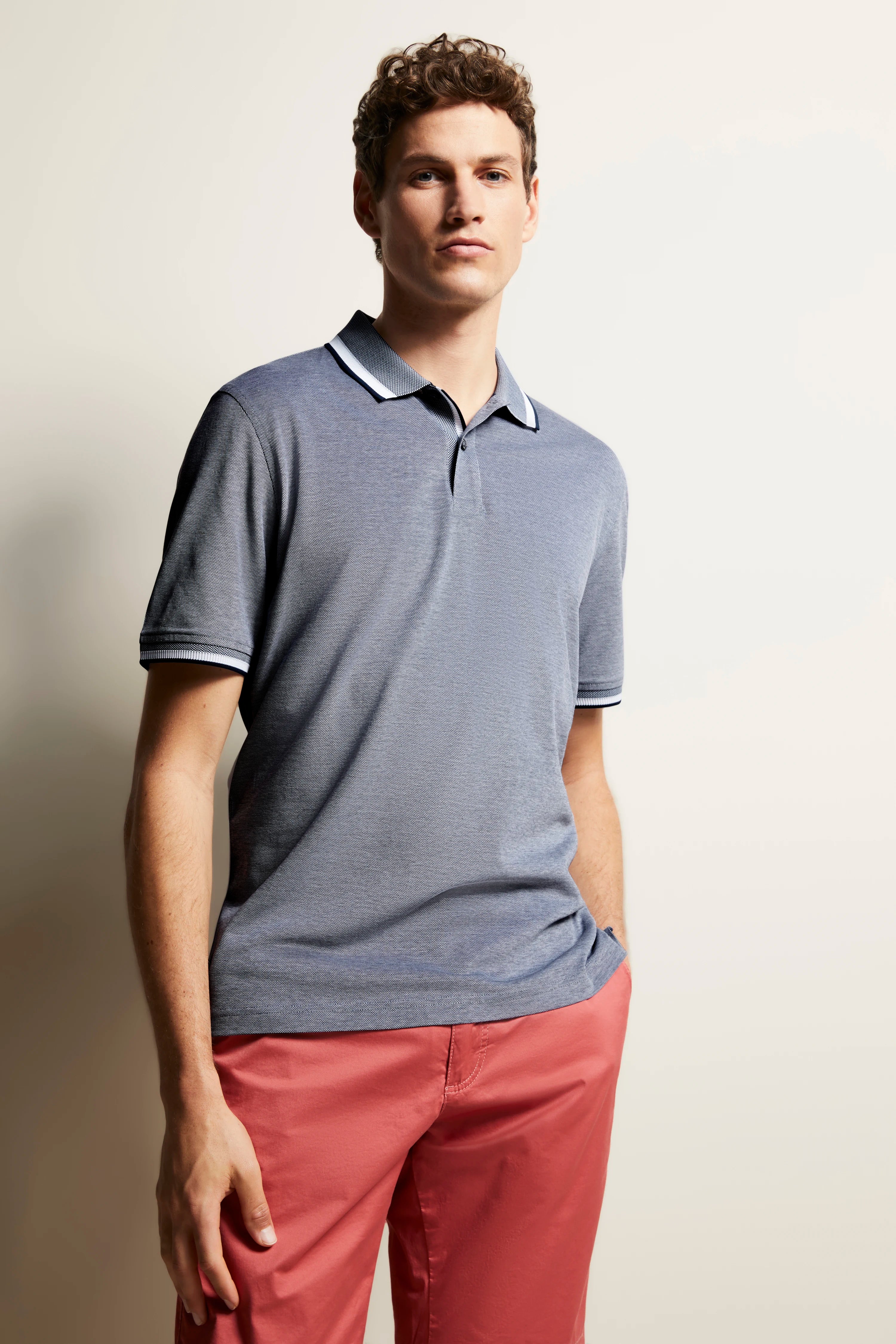 Blue bugatti polo shirt, red pants, model posing relaxed, hands in pockets.