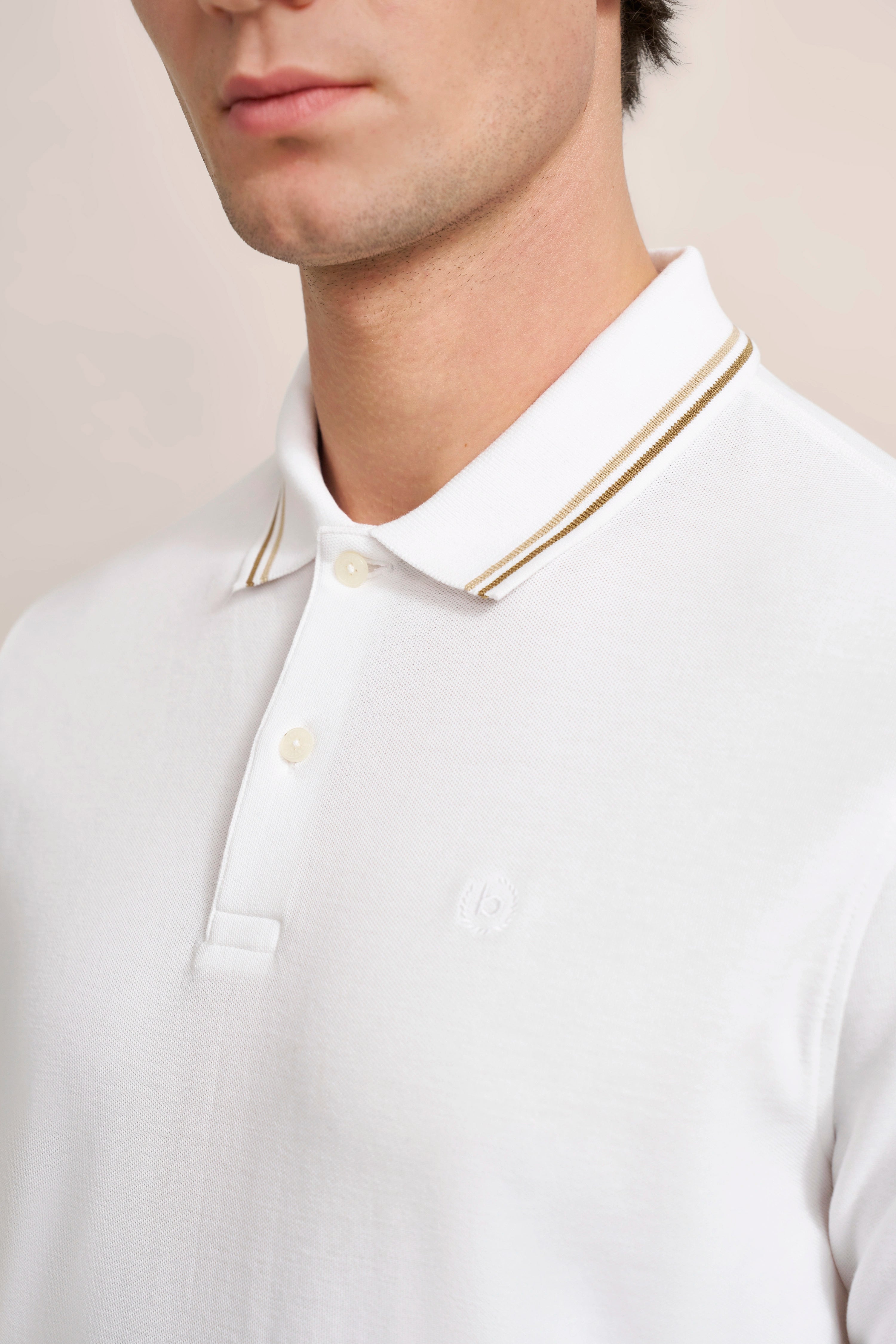 Weißes bugatti Poloshirt mit goldenen Streifen am Kragen, Modelbild, dezentes Posing.