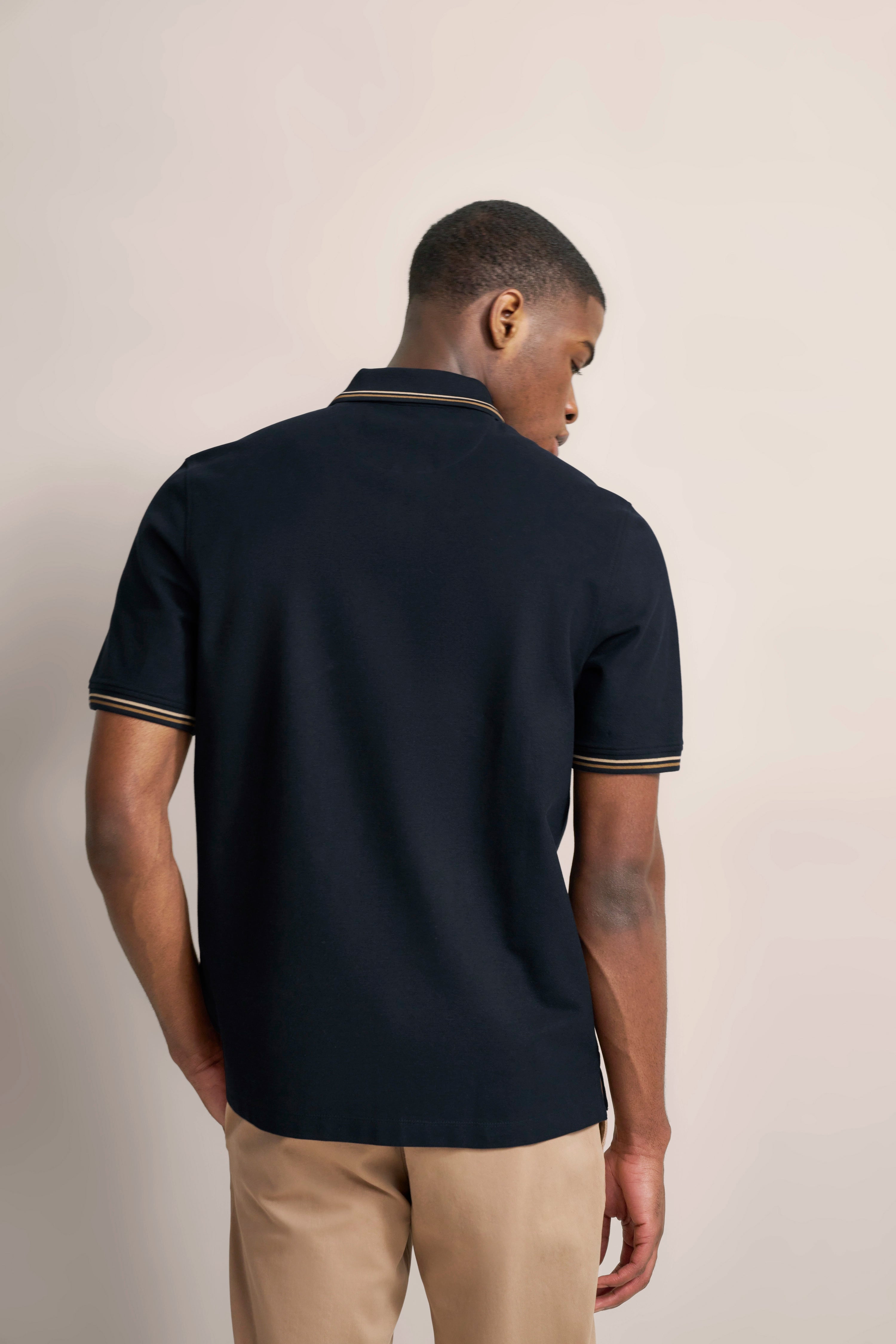 Zwart bugatti poloshirt, beige bies, beige broek, model van achteren in ontspannen pose.