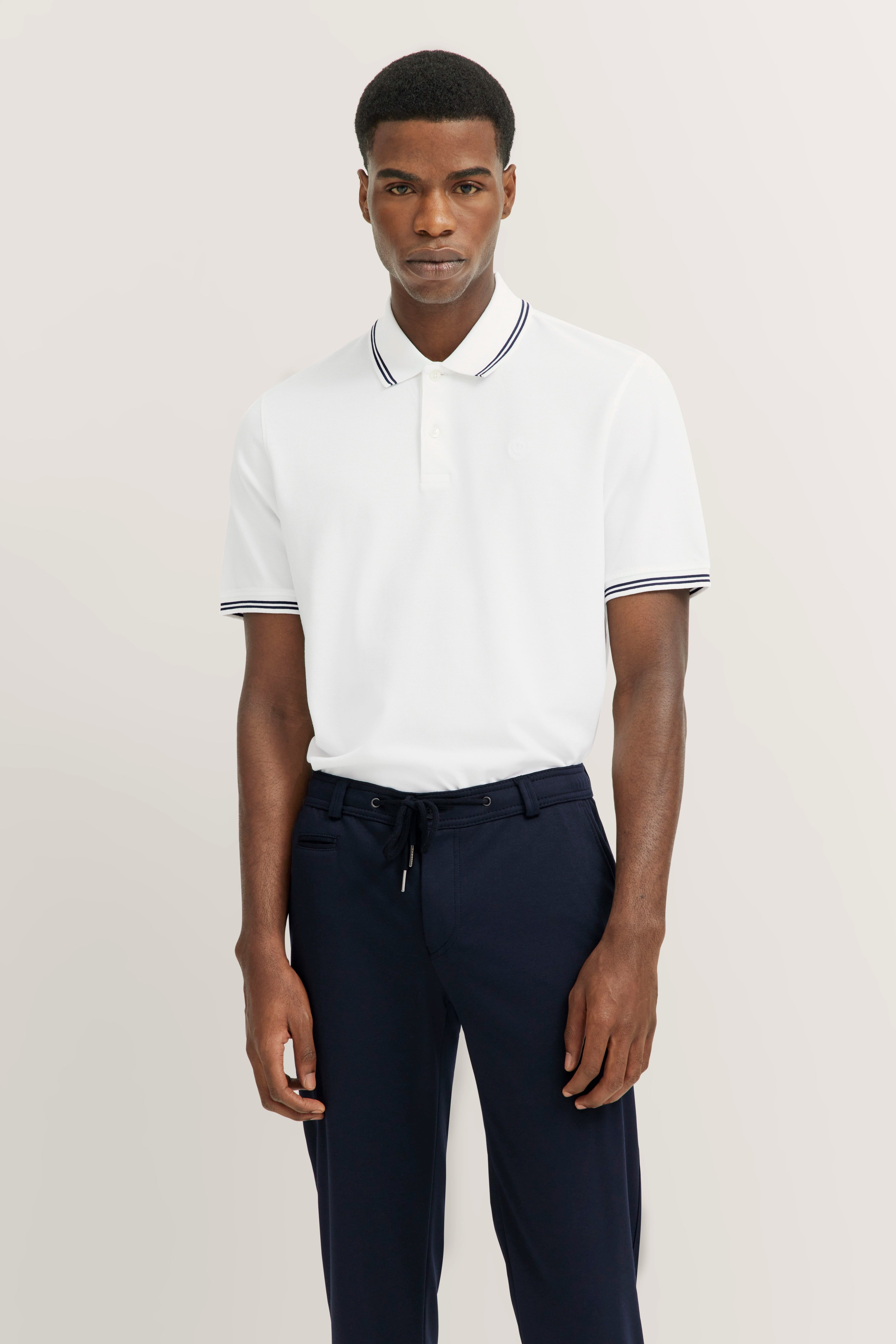 White bugatti polo and navy pants, model in a relaxed pose.