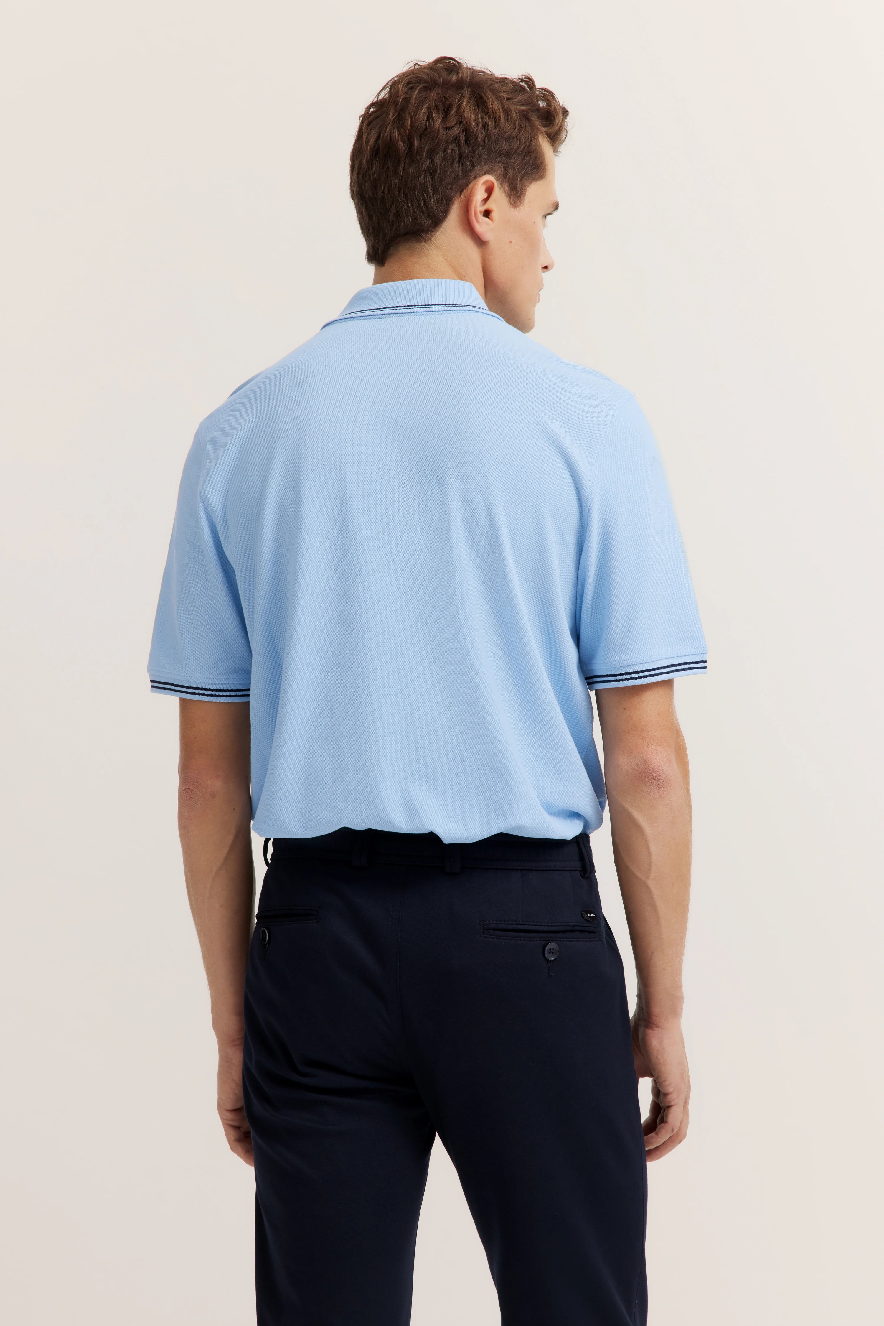 Men's outfit with light blue polo, navy pants, back view, model image, relaxed posture.