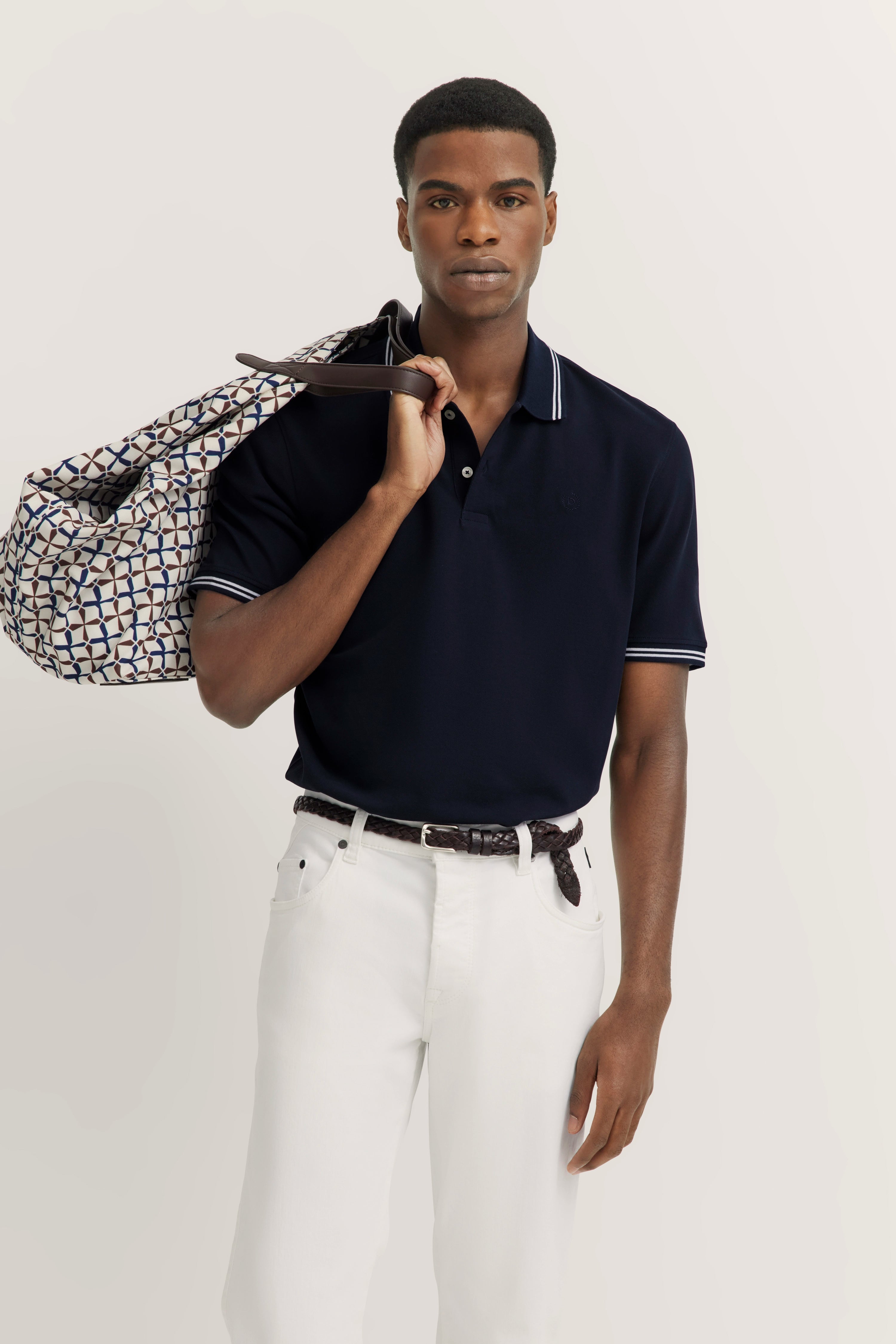 Black polo, white pants, patterned bag, model standing relaxed, embodying bugatti style.