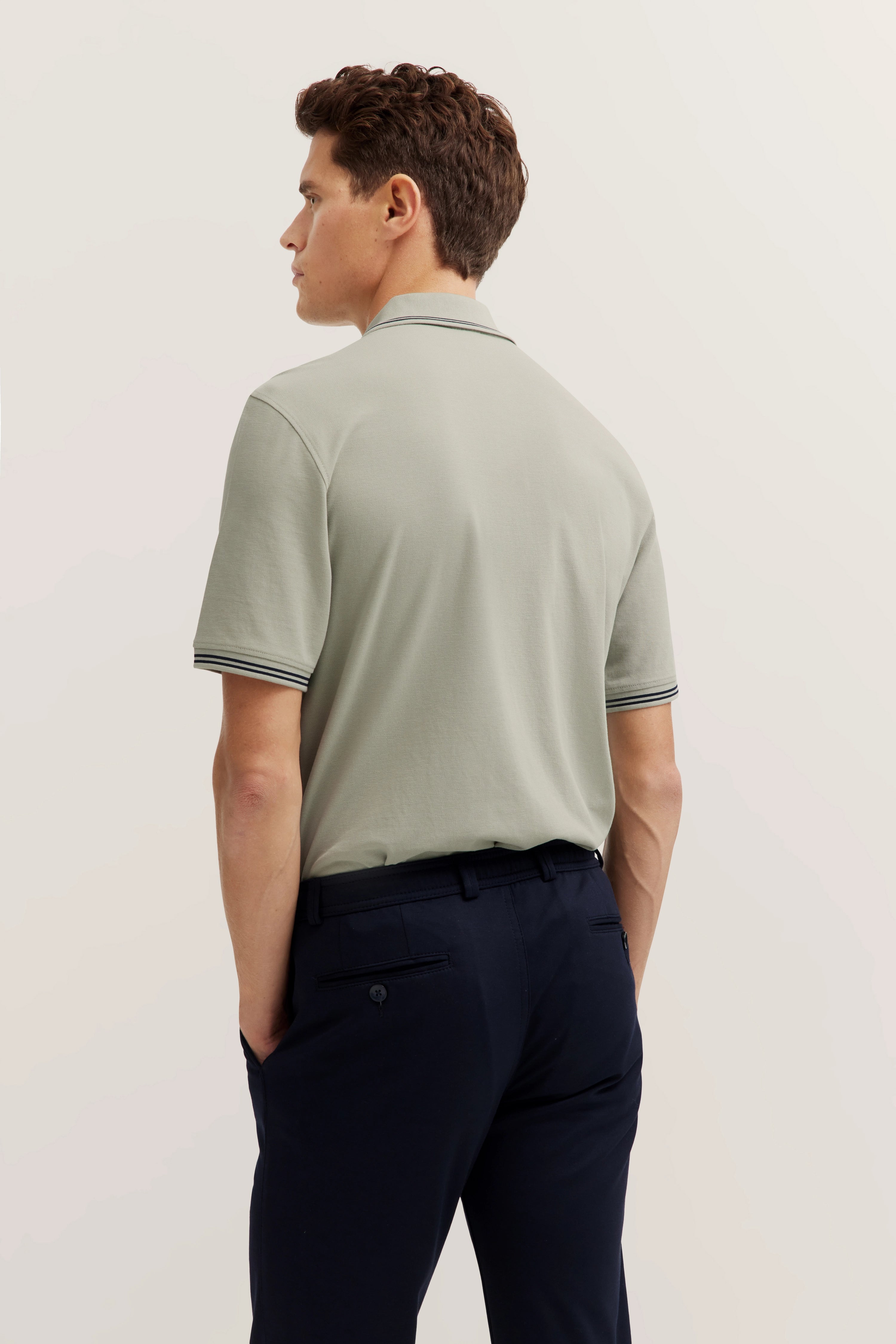 Man in beige bugatti polo, navy pants, side profile, relaxed pose.
