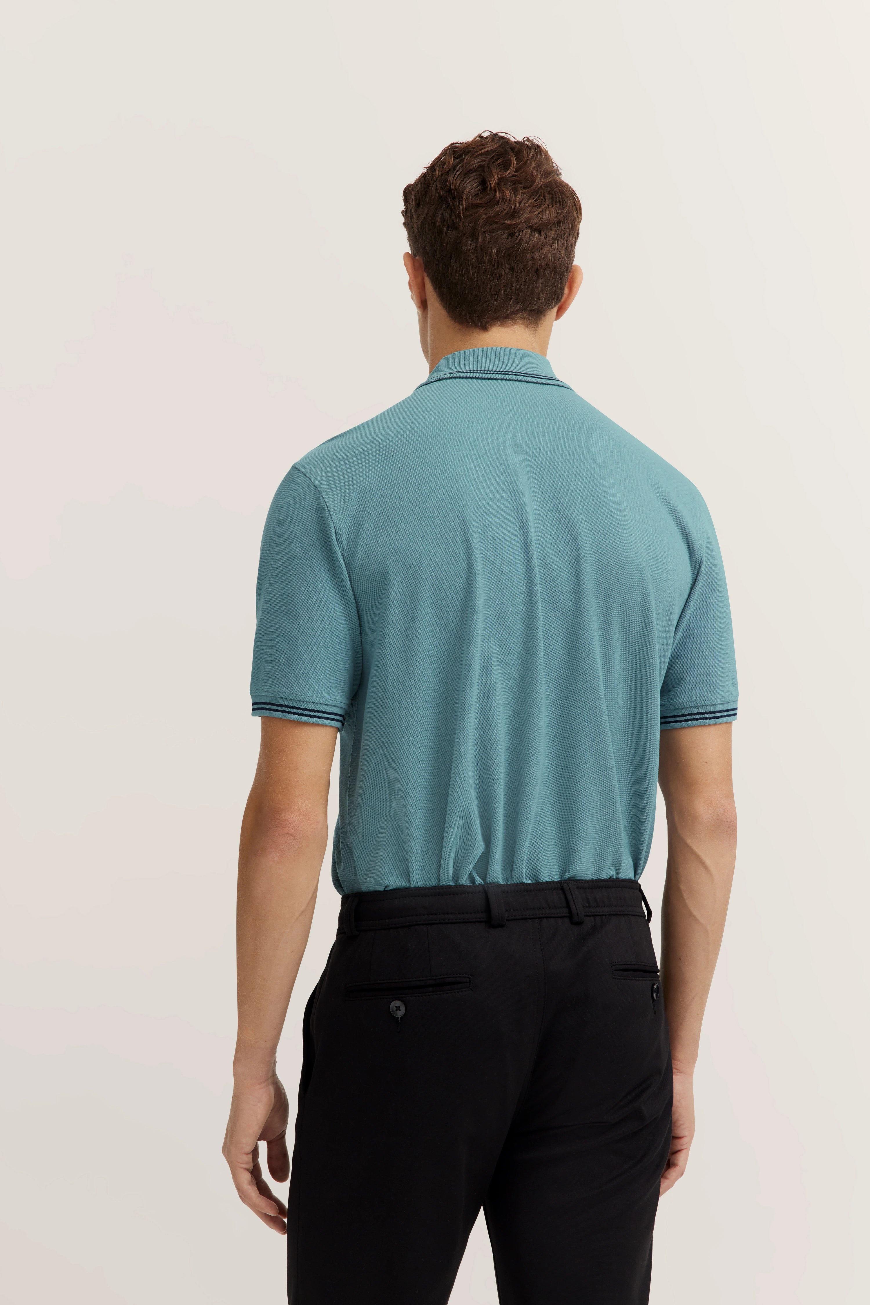 bugatti model, man in turquoise polo and black pants, back view.