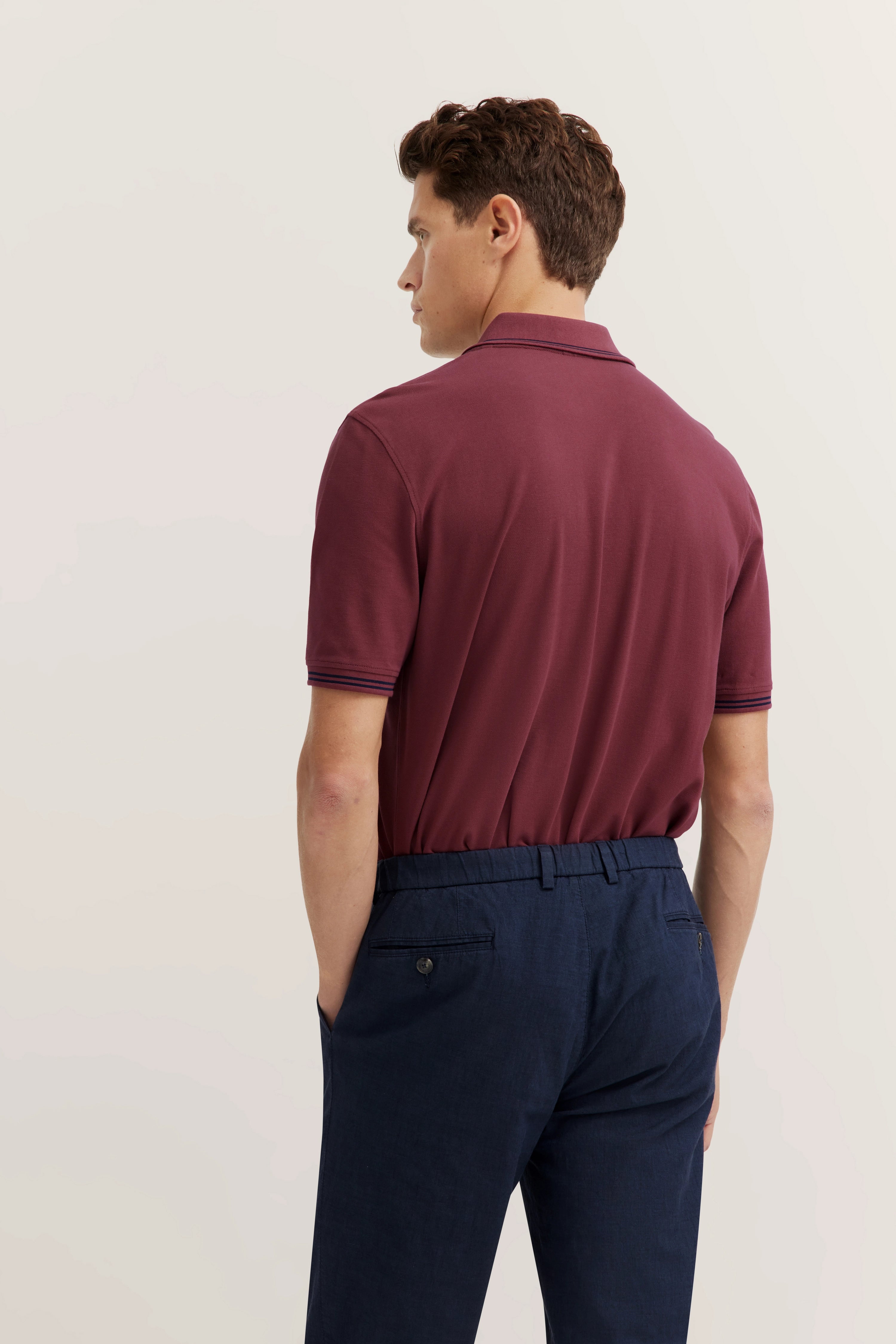Bordeaux polo shirt and blue trousers, model from back, relaxed stance, bugatti style.